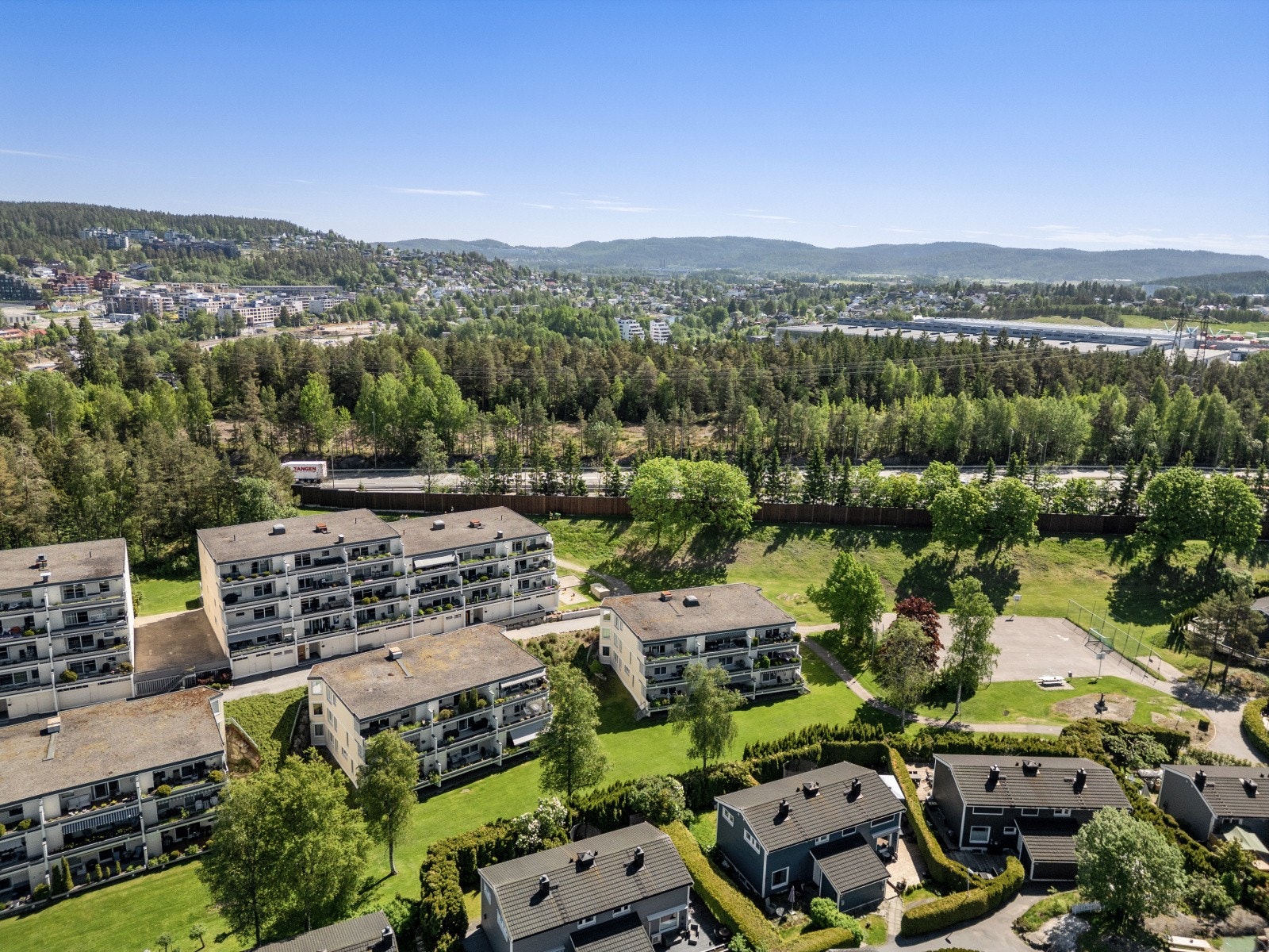 Dronebildene viser borettslagets attraktive plassering med åpne grøntområder, god avstand mellom bebyggelsen og en luftig atmosfære. Her får du følelsen av å bo landlig og fredelig, samtidig som byen aldri er langt unna. Galleribilde