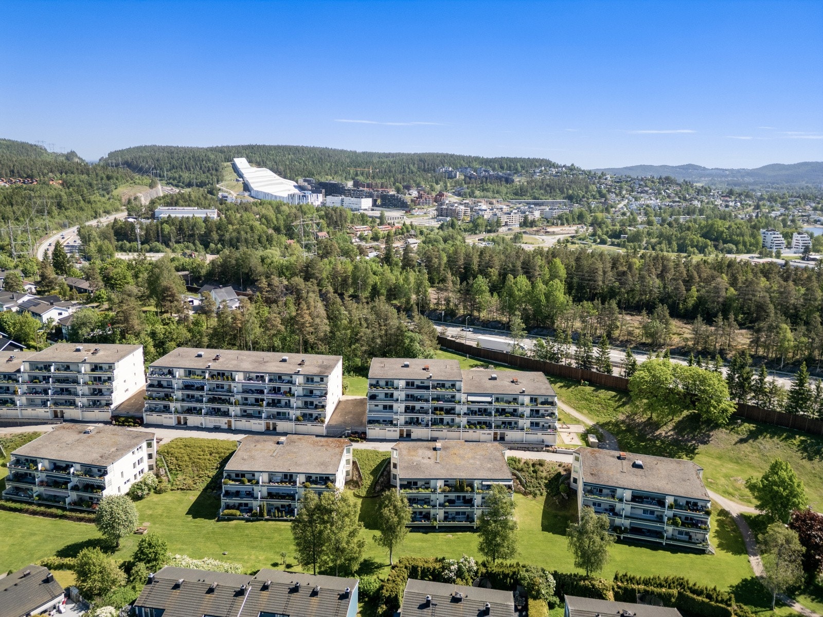 Fra området kan du nyte utsyn over grønne omgivelser og nærliggende bebyggelse. På flere av dronebildene skimtes også SNØ, som tilbyr helårs ski- og aktivitetsmuligheter. Galleribilde