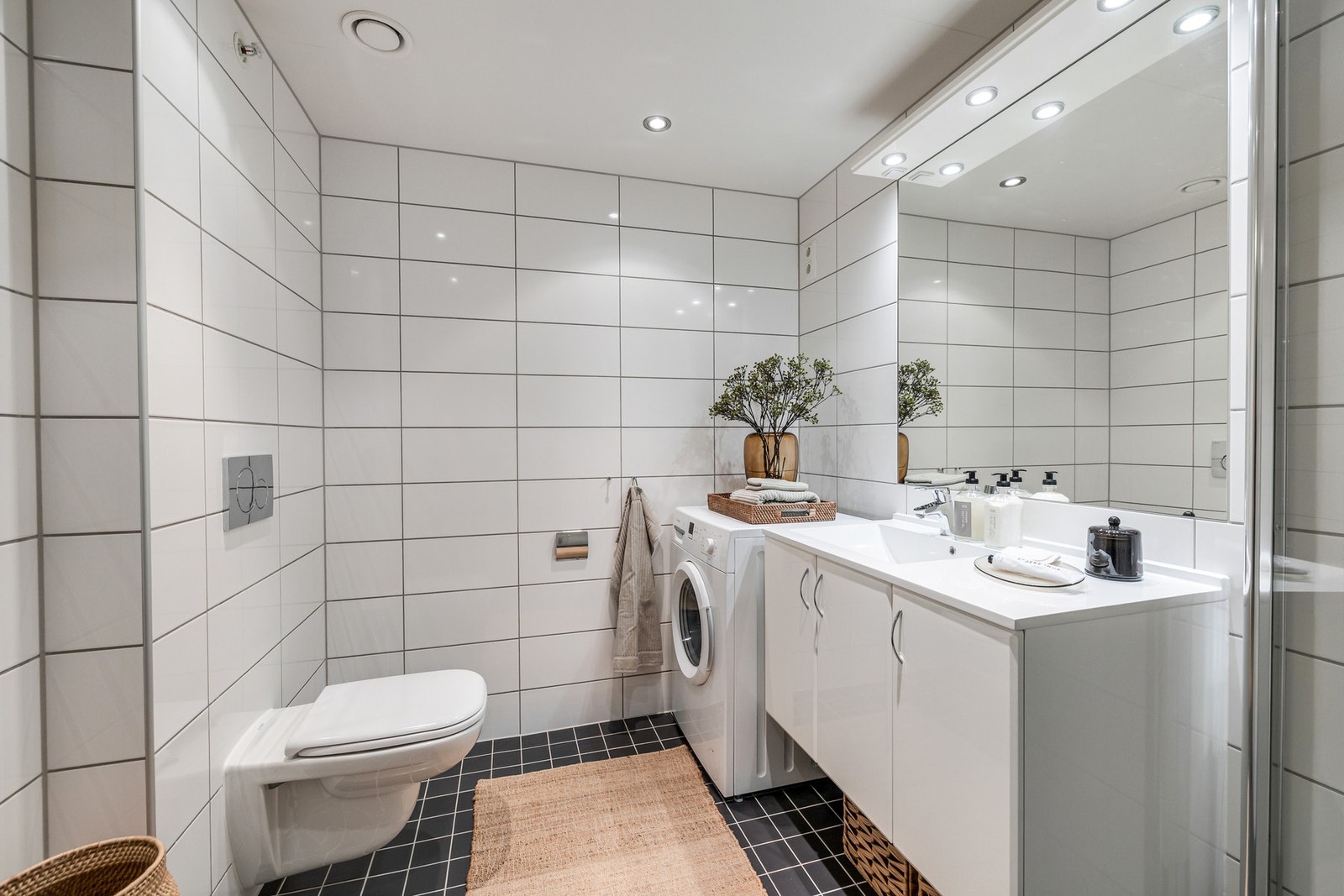 Badet har dusjhjørne med innfellbare dusjdører i glass, stort, vegghengt servantskap, vegghengt toalett og opplegg for vaskemaskin og tørketrommel Galleribilde