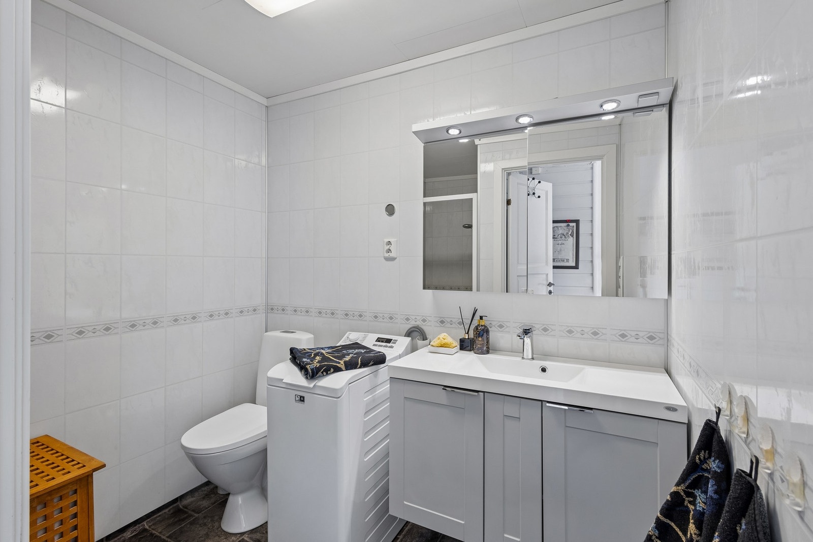 Badet er fra 2002, med vinylbelegg på gulvet og baderomsplater på veggene. Lyst baderom med baderomsinnredning med underskap, servant og speilskap med belysning. Galleribilde
