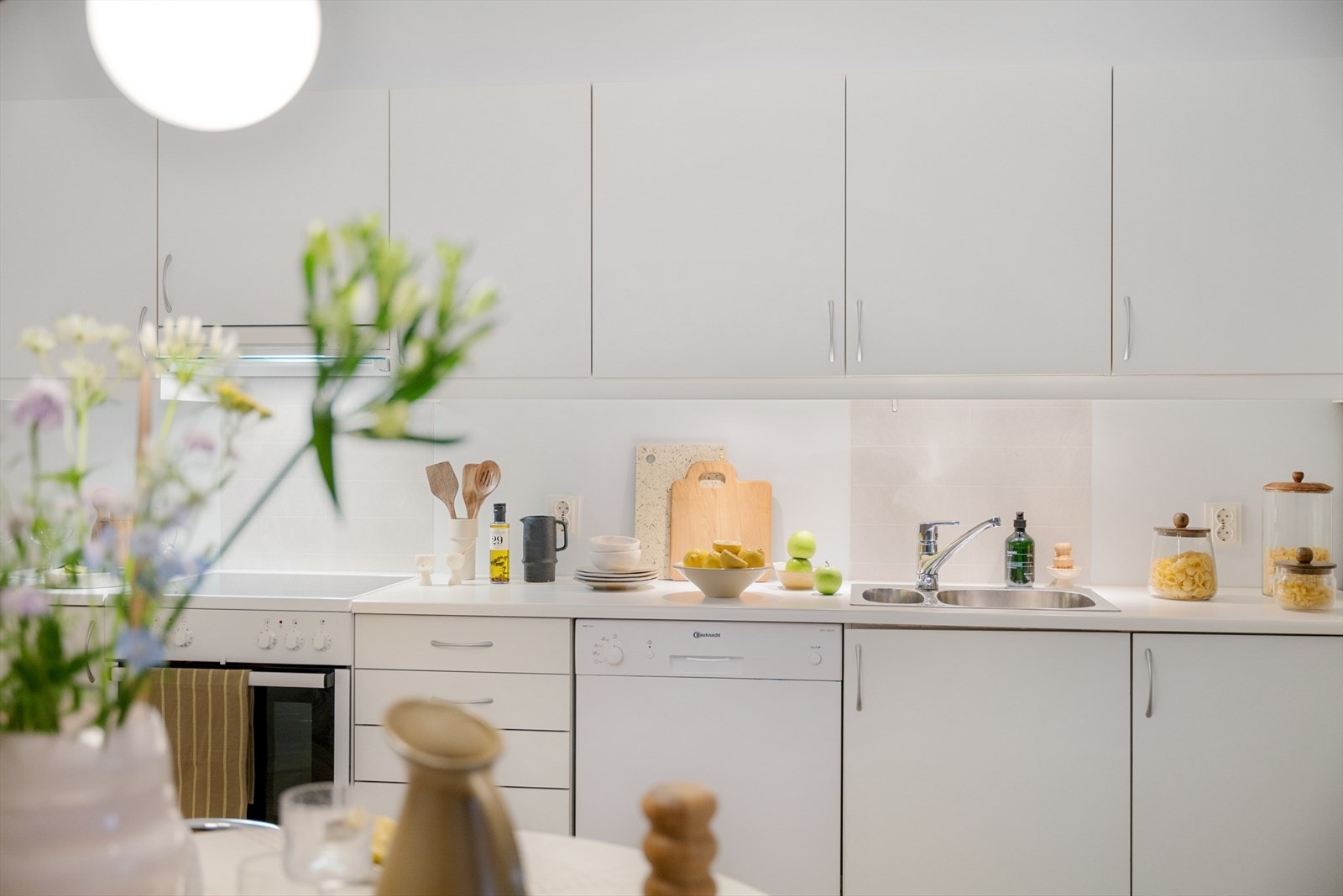 Kjøkkeninnredningen fra Sigdal er stilren med hvite, glatte fronter og laminat benkeplate. Hvitevarer som oppvaskmaskin, komfyr og kjøleskap medfølger. Galleribilde