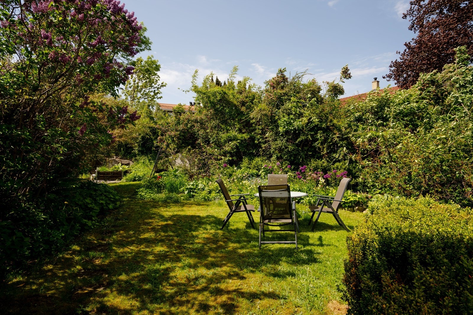 Hagen gir et grønt og innbydende preg med variert vegetasjon, prydbusker, blomsterbed og naturlige soner som skaper en lun og privat atmosfære. Galleribilde