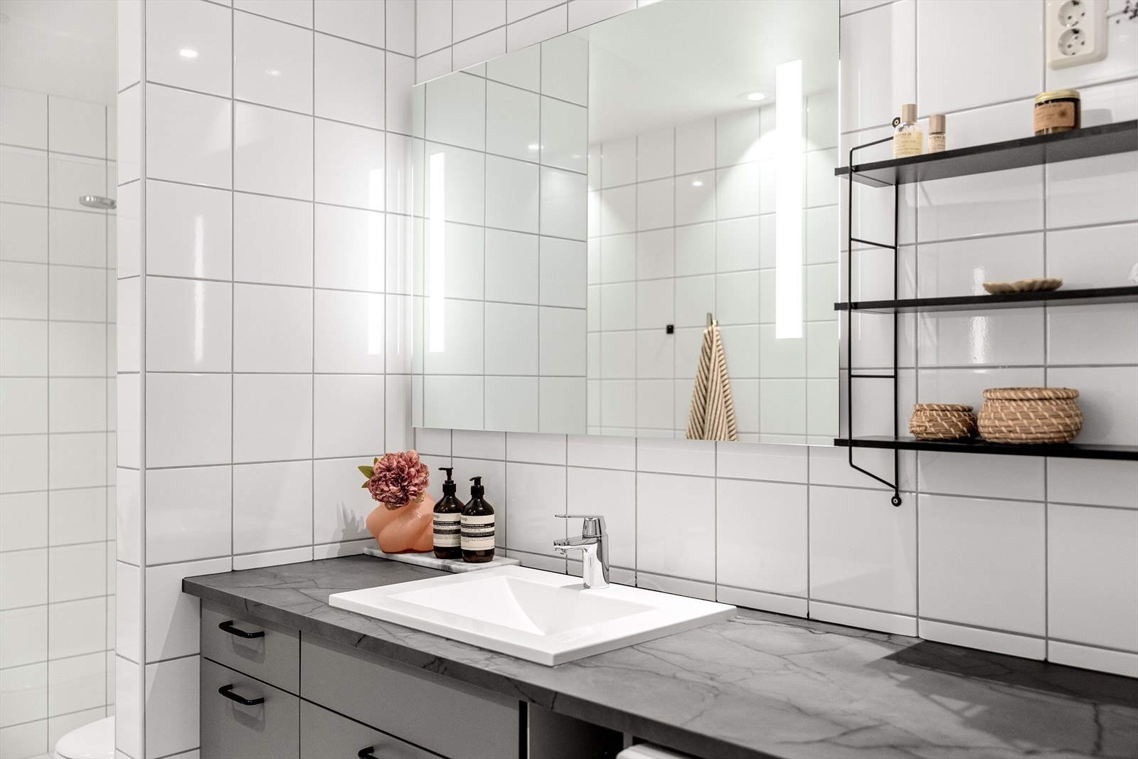 Badet er innredet med vegghengt toalett med innebygd sisterne, servant nedfelt i innredning, dusjhjørne med svingbare glassdører og mekanisk avtrekk. Det er opplegg for vaskemaskin. Galleribilde