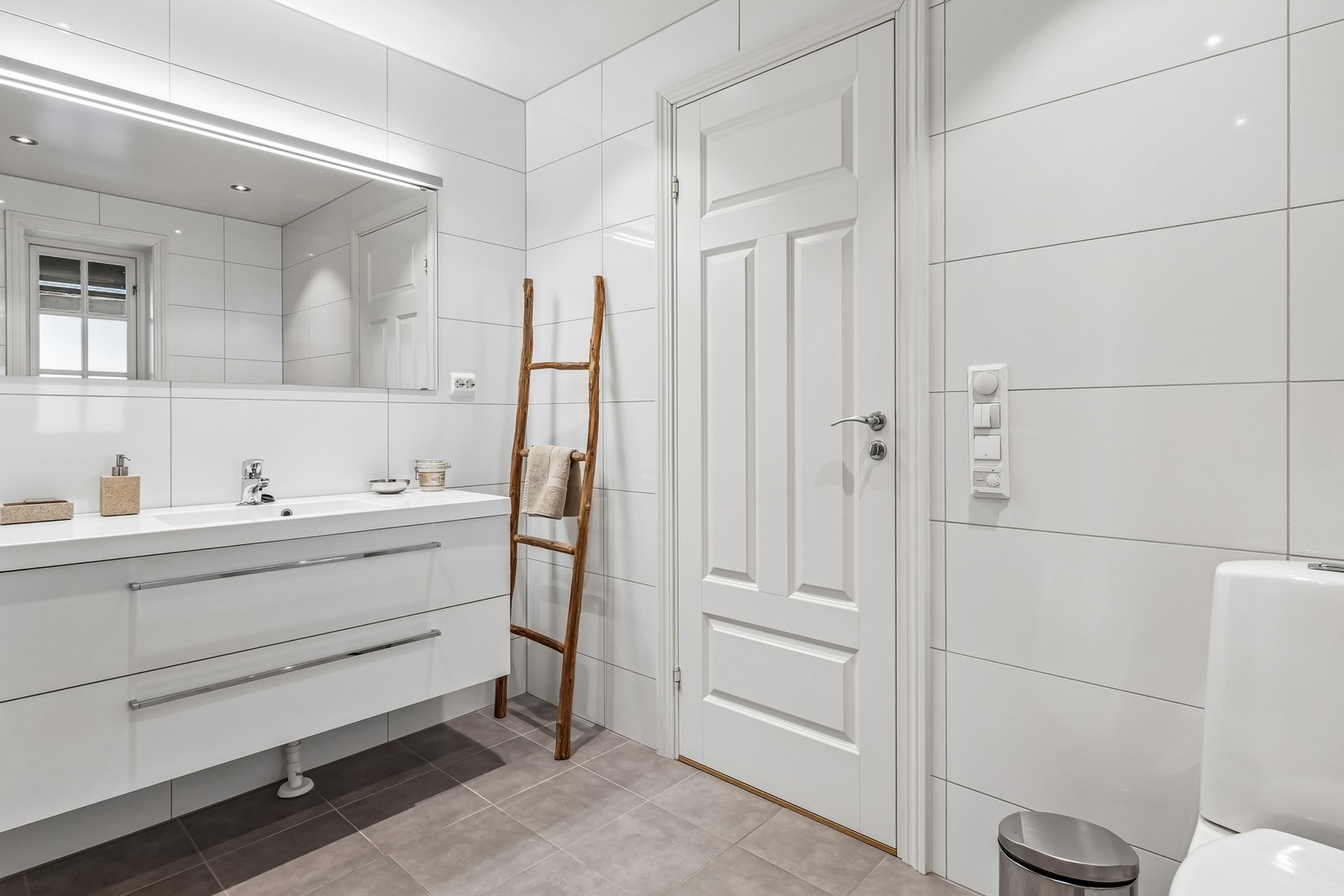 Badet er romslig og flislagt med lyse rektangulære fliser på vegg samt gråe kvadratiske på gulv Galleribilde