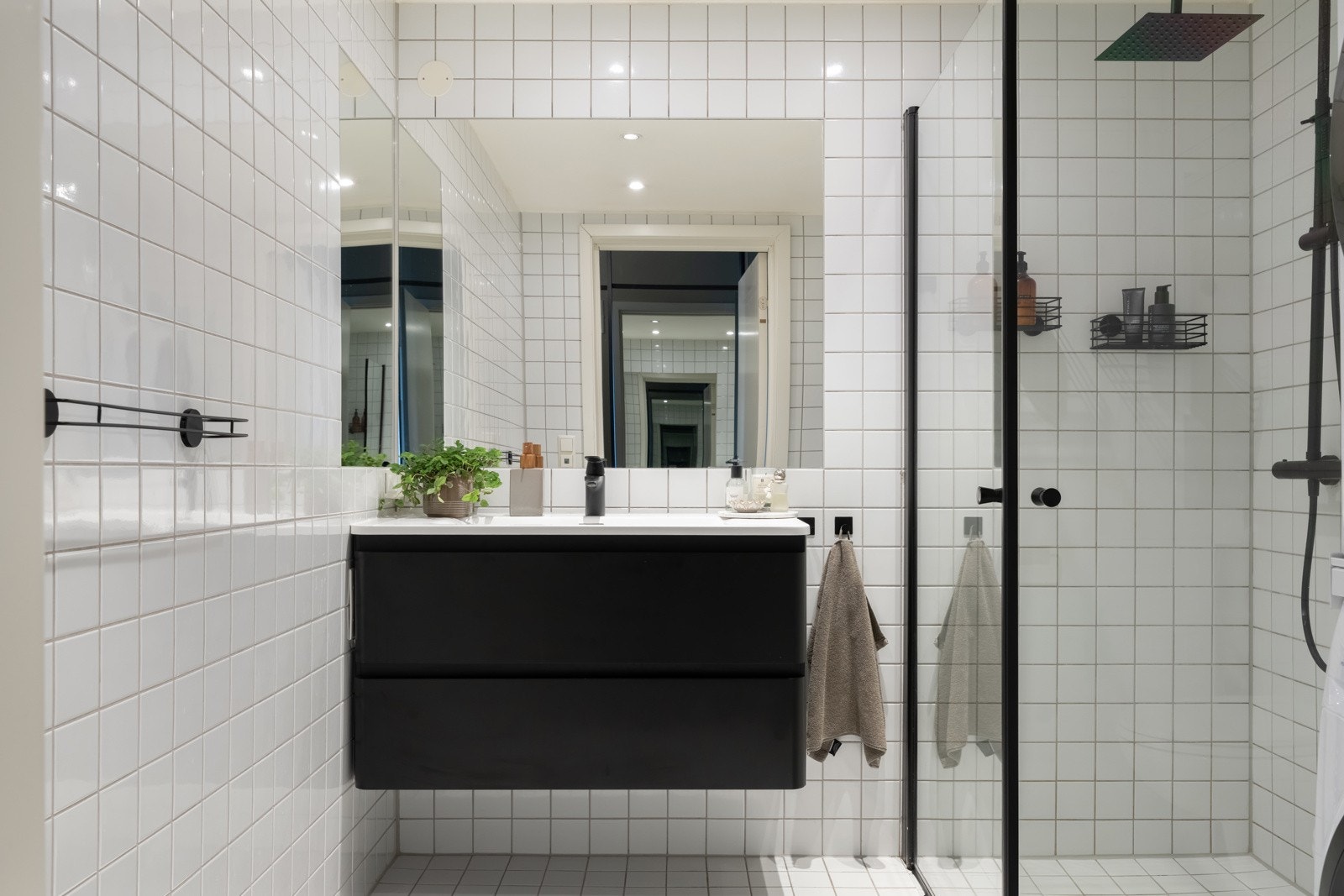 Badet inneholder dusjhjørne med veggmonterte dusjdører og blandebatteri, innredning med heldekkende servant, speil og veggmontert klosett. Galleribilde