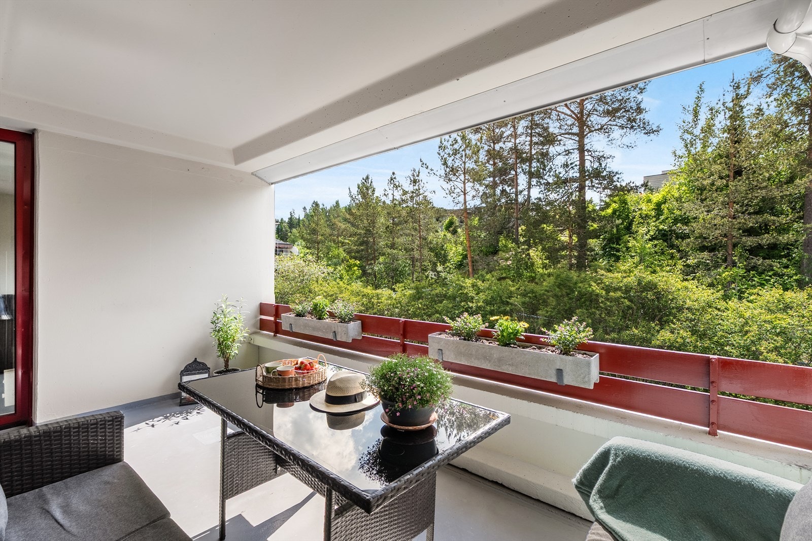 Utsikten går mot usjenerte grønne omgivelser, og plantekassene langs rekkverket gir en frodig ramme. Galleribilde