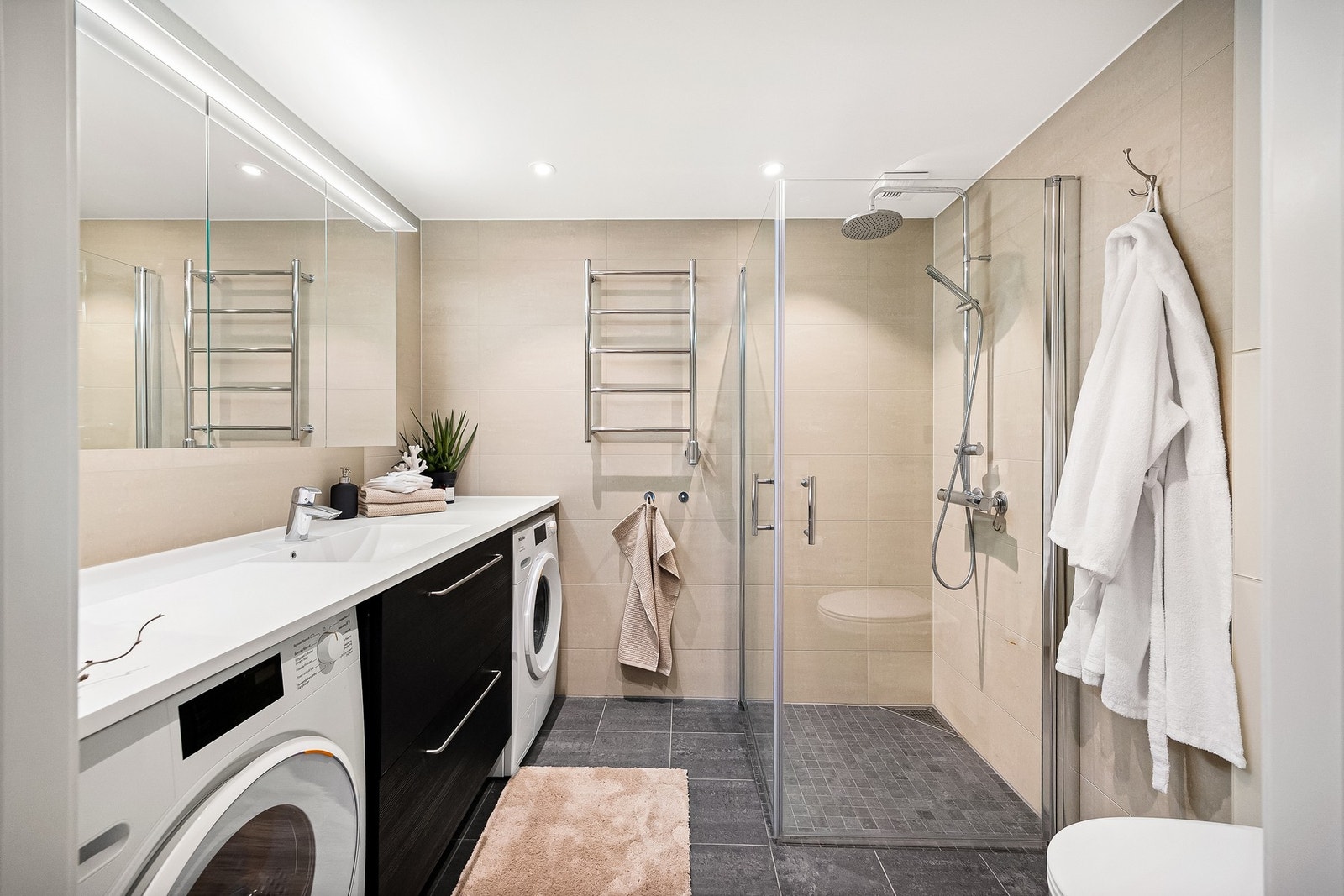 Badet er en prefabrikkert baderomsmodul fra 2022 og fremstår lekkert og moderne. Flislagte overflater, vannbåren gulvvarme og innfelte downlights i himling. Galleribilde