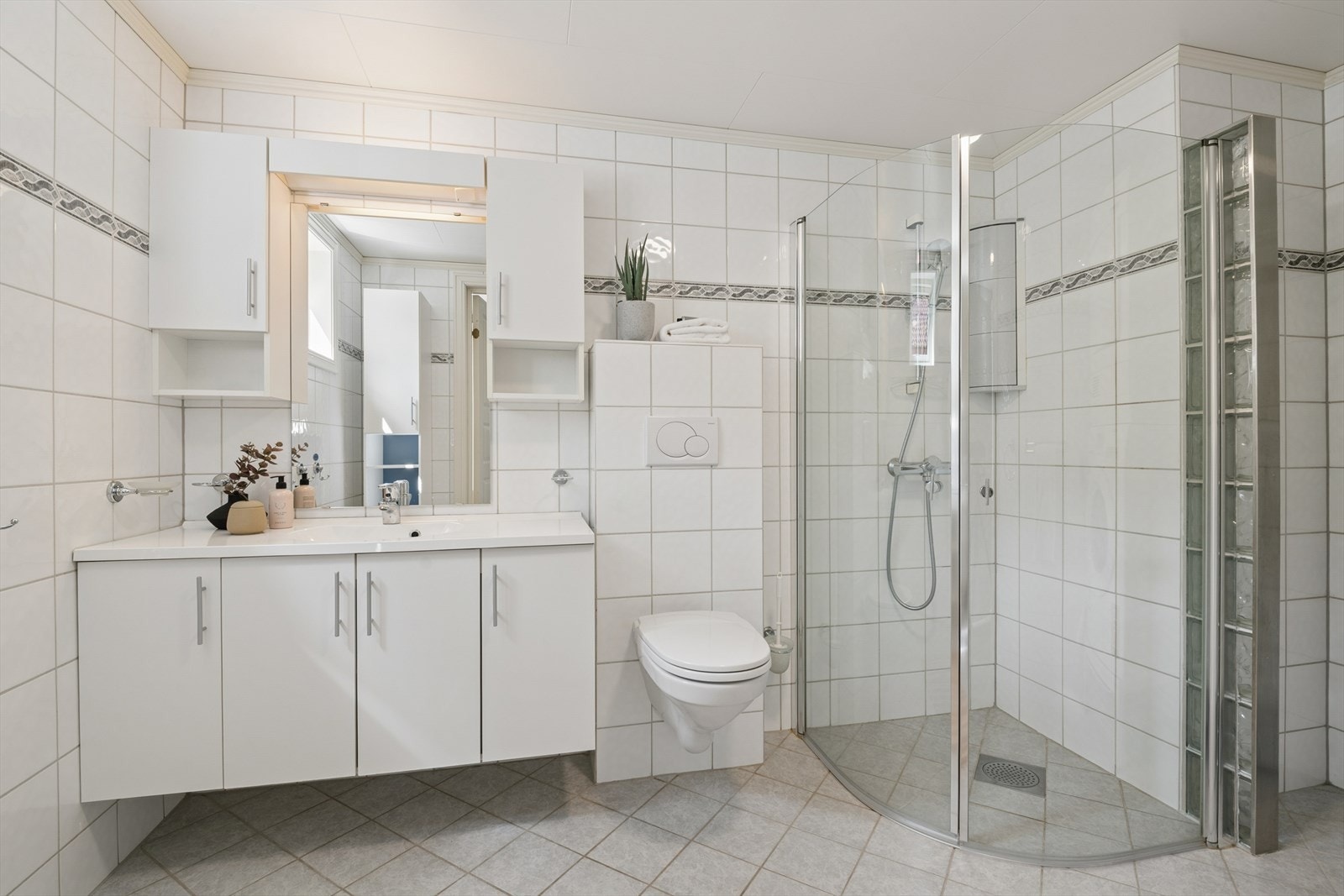 Romslig bad med dusjhjørne, vegghengt toalett og godt med oppbevaringsplass. Det er opplegg for vaskemaskin. Galleribilde