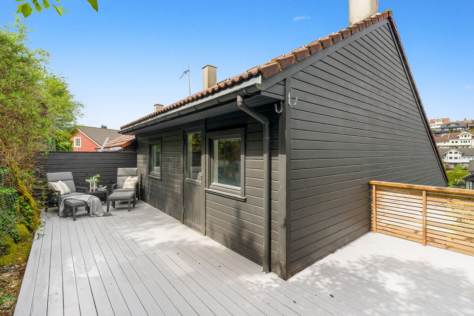 På baksiden ligger en hyggelig terrasse som strekker seg langs boligen, med plass til utemøbler, loungestoler og grønne innslag. Galleribilde