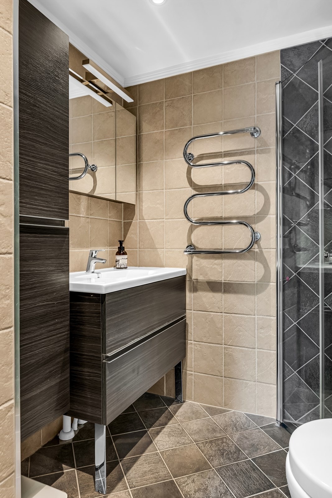 Badet er utstyrt med servantinnredning, speilskap med belysning, vegghengt høyskap, vegghengt toalett og dusjhjørne med svingbare glassdører. Galleribilde