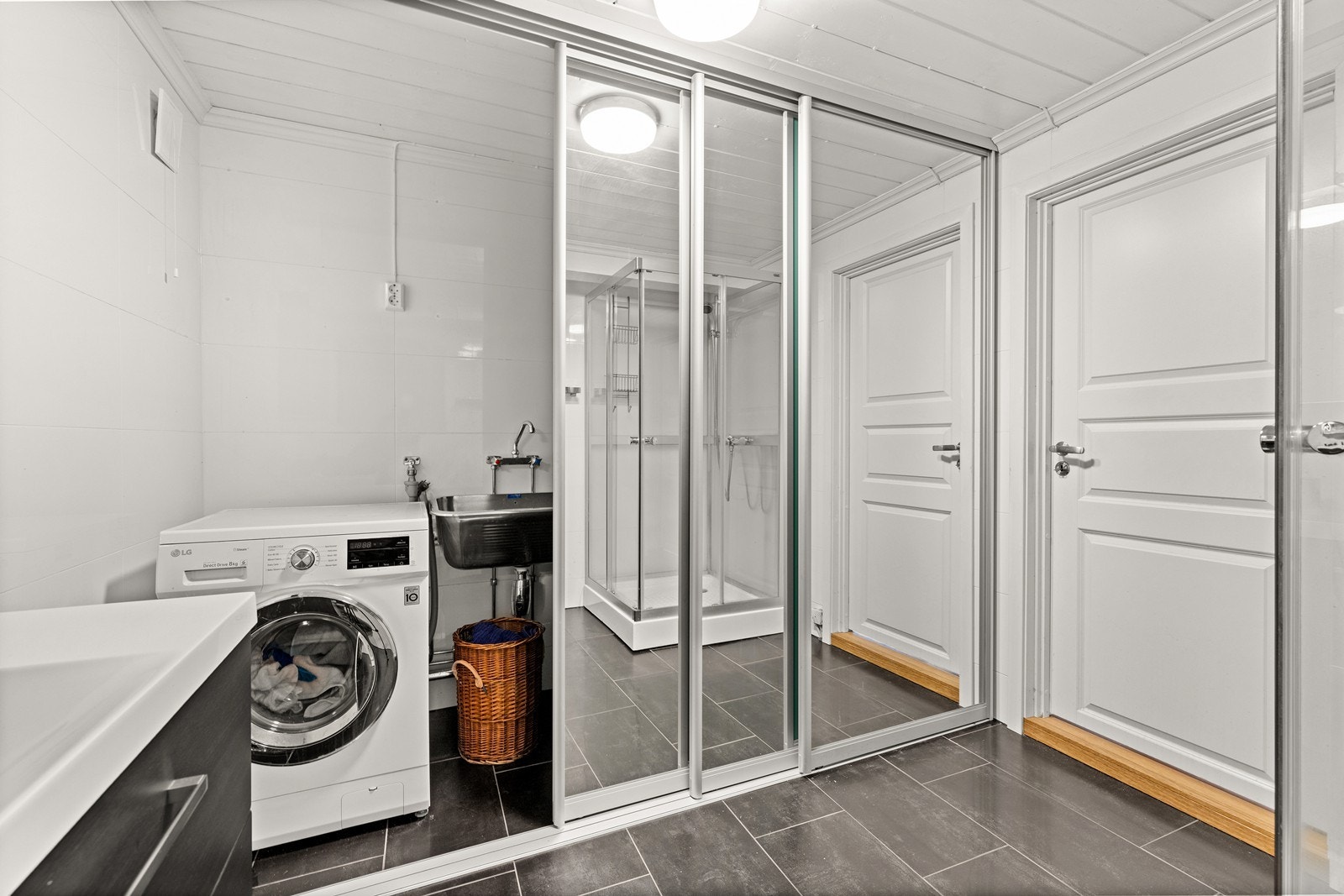En stor skyvedørsgarderobe med speilfronter skjuler vaskemaskin, skyllekar og oppbevaring. Galleribilde