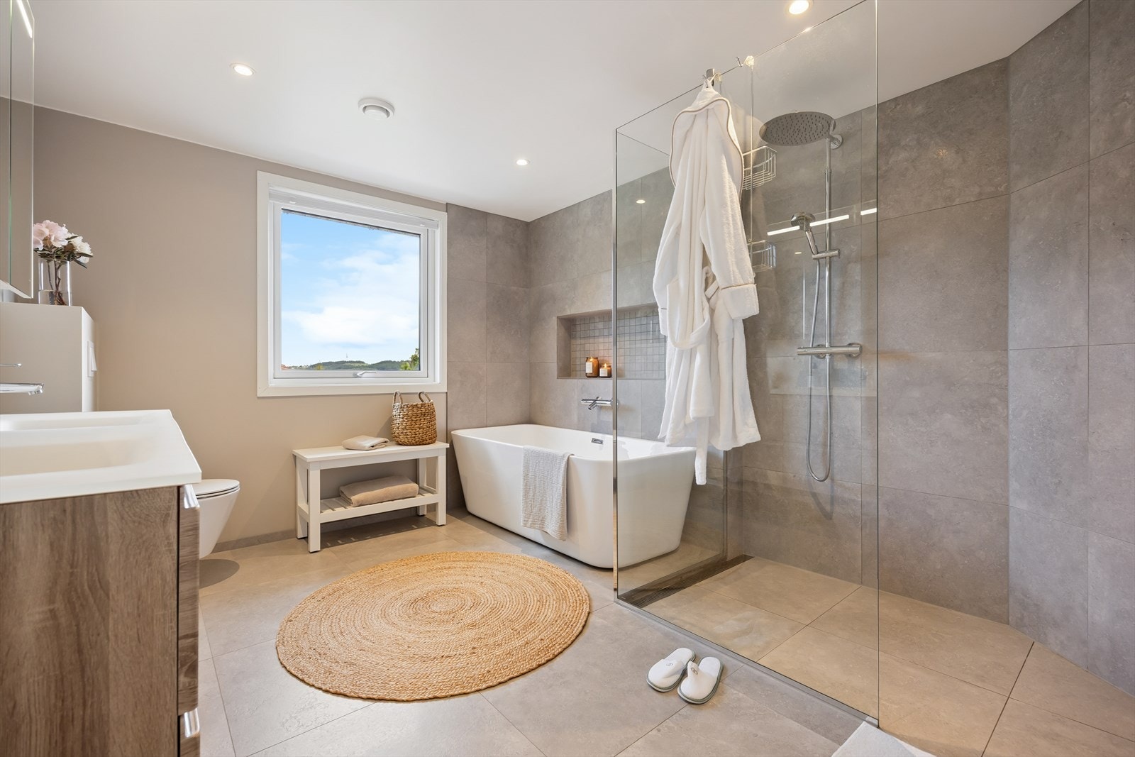 Badet, oppgradert i 2021, fremstår som moderne og delikat med store fliser, romslig dusjsone med glassvegger og rainshower, badekar med innfelt nisje, samt baderomsinnredning med god oppbevaringsplass og toalett. Galleribilde