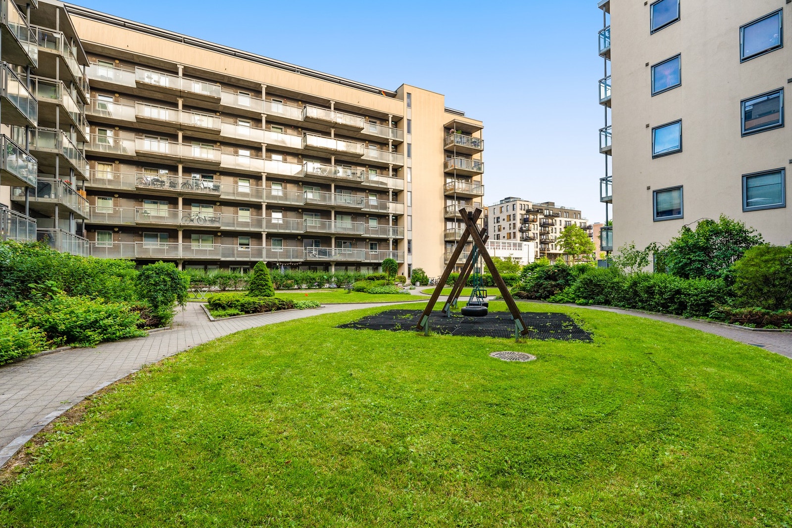Felles tomt opparbeidet med blant annet belegningsstein, terrasse på terreng, lekeplass, sittegrupper, plenarealer og andre forskjellige beplantninger. Galleribilde