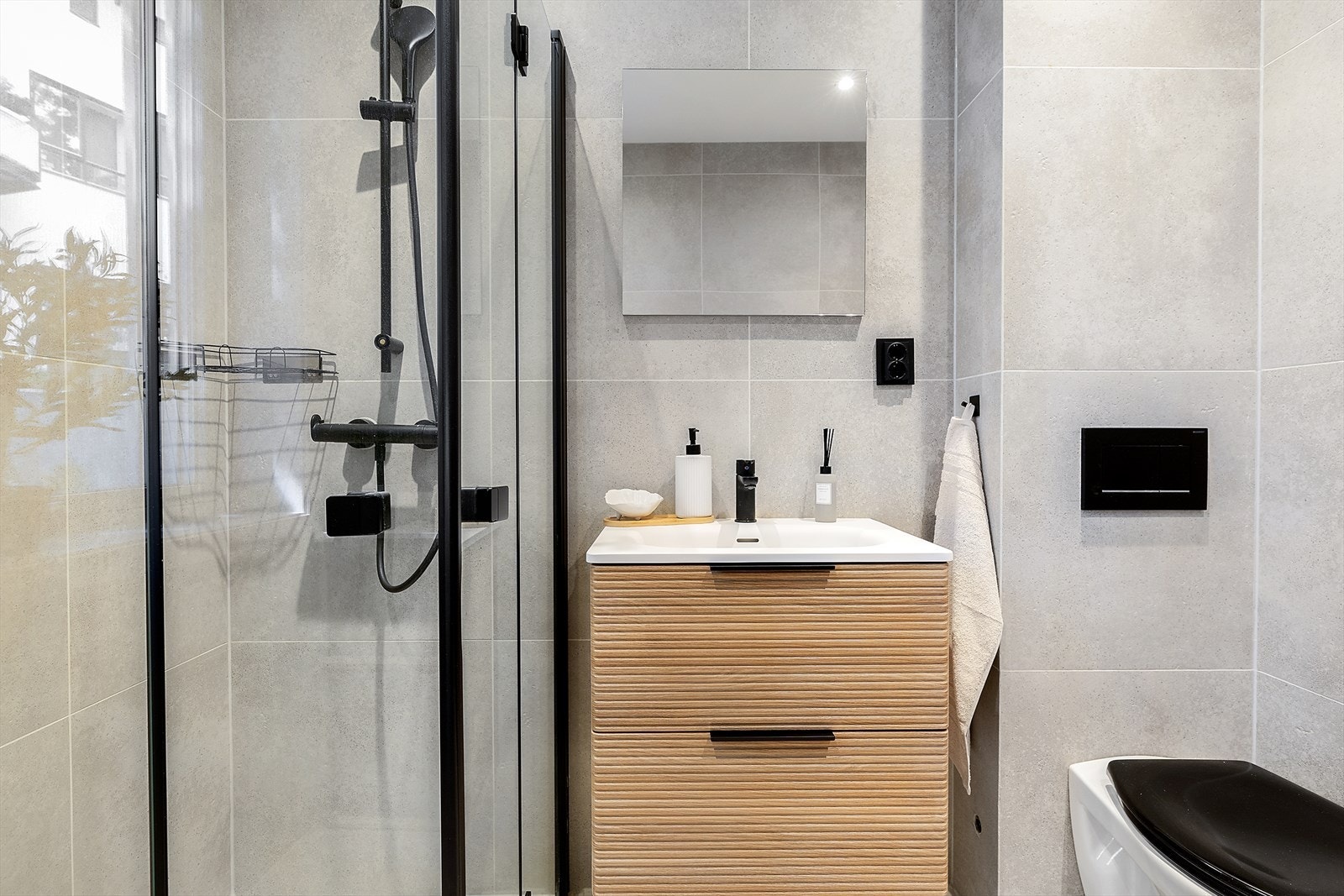 Badet har flislagte gulv og vegger og er utstyrt med ny baderomsinnredning, dusj med innfellbare dører i herdet glass, servant og veggfestet klosett med innebygget sisterne. Varmekabler i gulv. Galleribilde