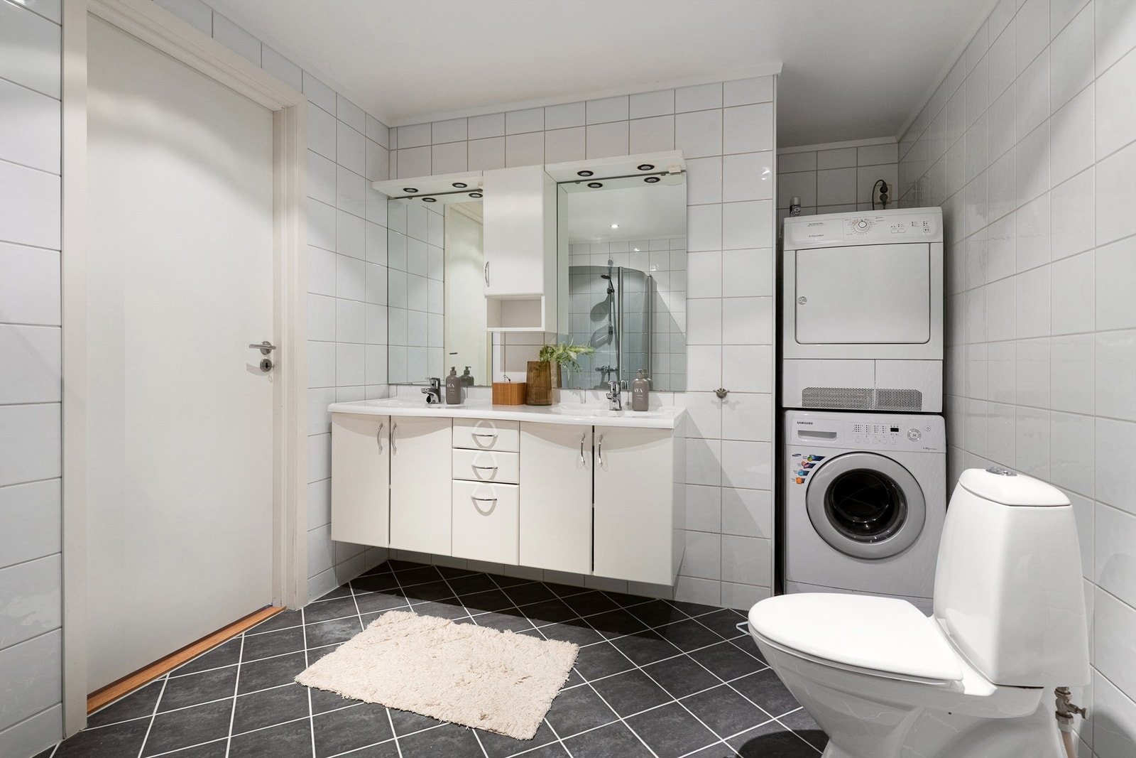 Lyst og moderne bad med integrert vaskemaskin og tørketrommel. Praktisk innredning og flislagte overflater gir et stilrent uttrykk. Galleribilde
