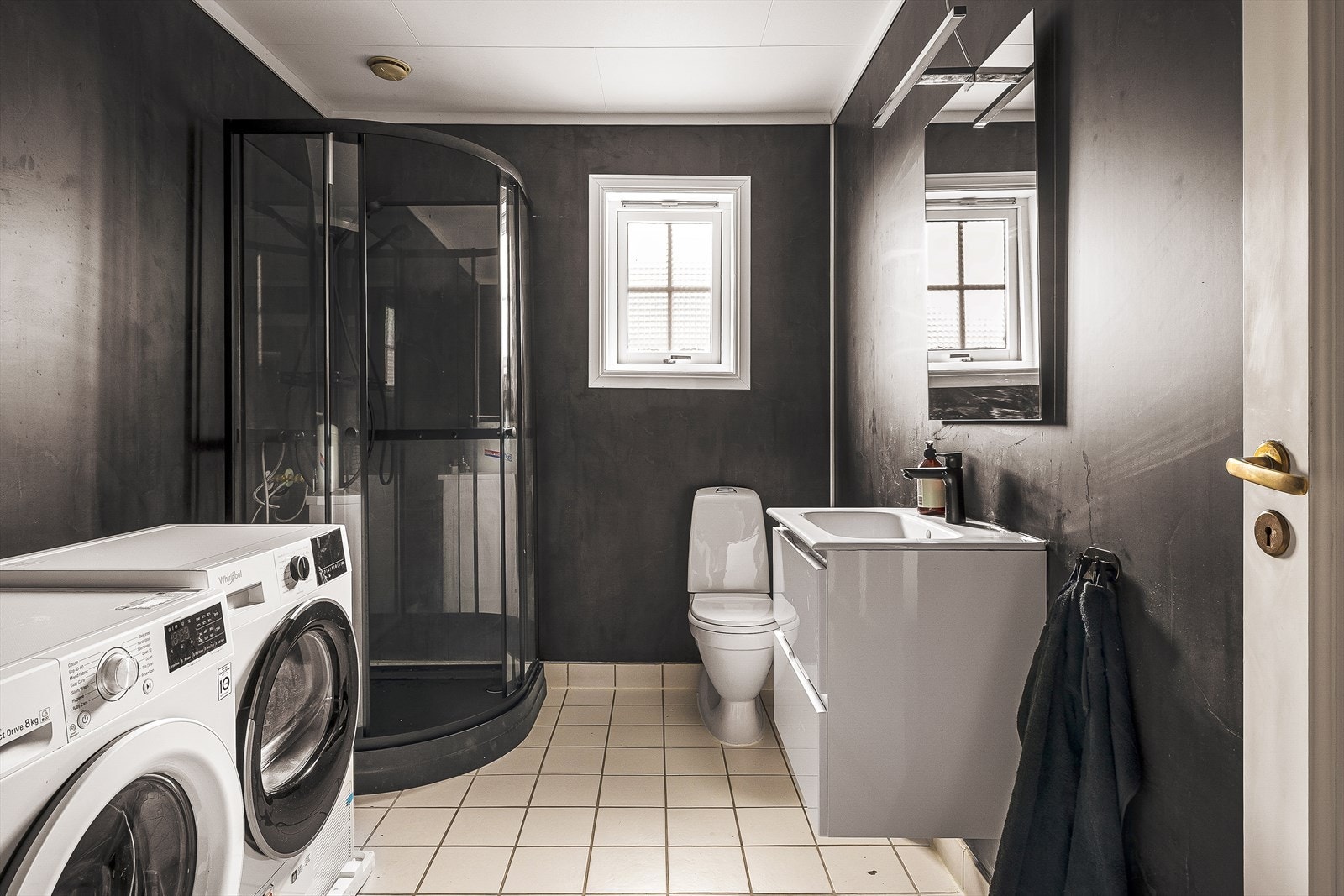 Badet har dusjkabinett, toalett og helstøpt servant.
Baderomsmøbler med slette fronter. Speil og lys over servant.
Opplegg for vaskemaskin. Baderomsplater på vegger og keramiske fliser på gulv med underliggende varmekabler. Galleribilde