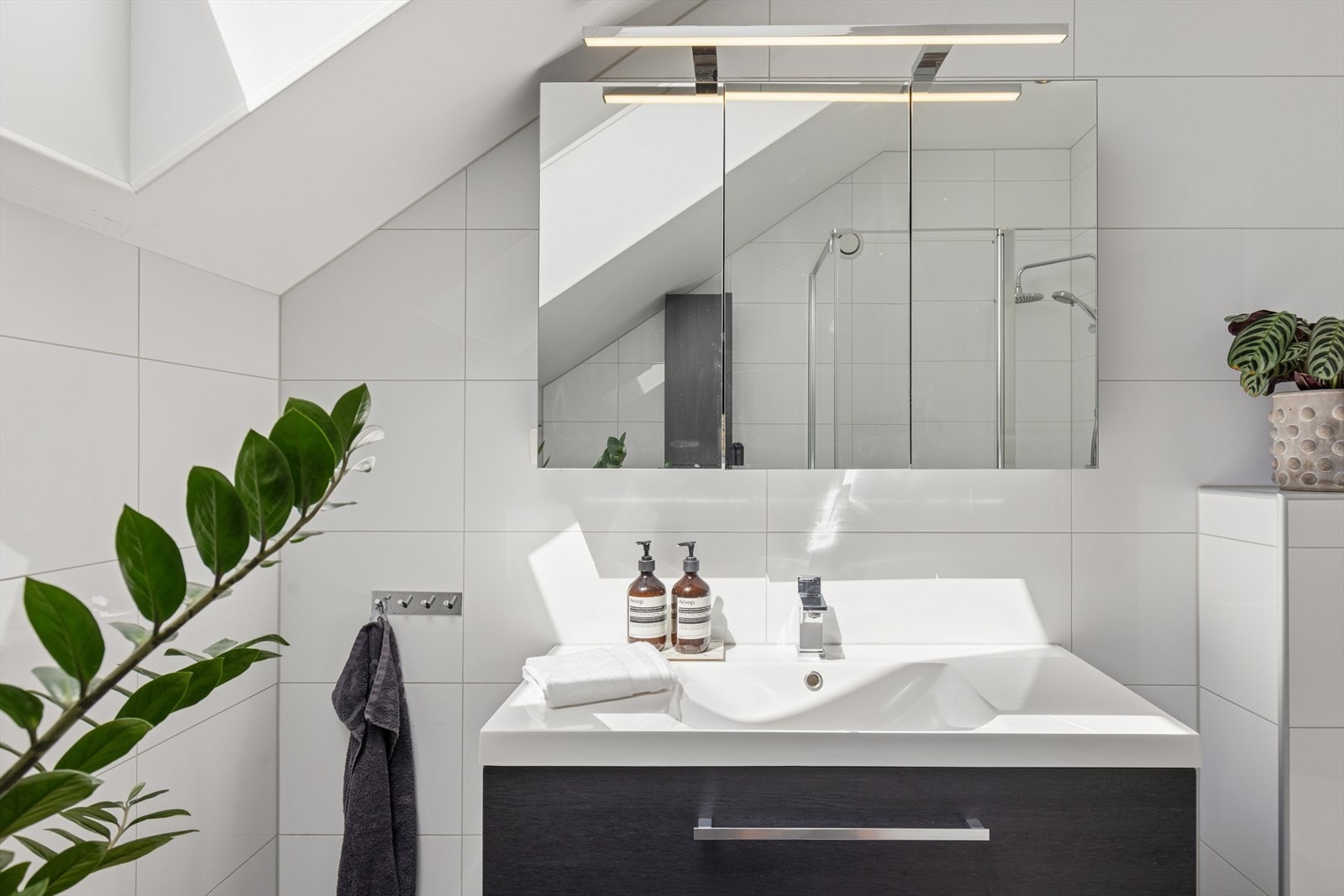 Badet på loftet har en innbydende utforming med flislagte overflater, elektriske varmekabler, servant, veggmontert toalett og dusjvegger, i tillegg til innfelte downlights som bidrar til en behagelig atmosfære. Galleribilde