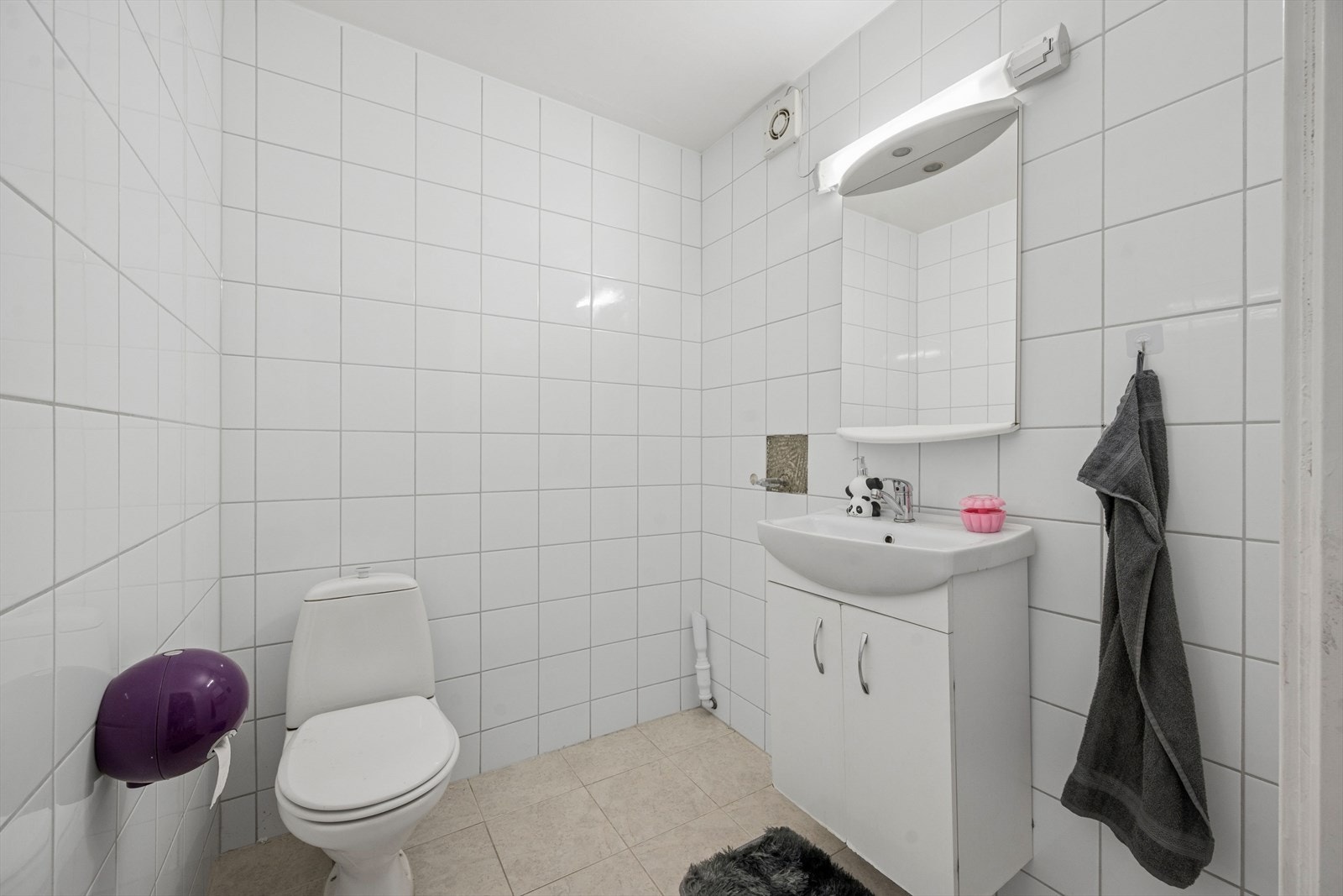 WC har fliser på gulv og vegger, og inneholder frittstående toalett og servant med underskap Galleribilde