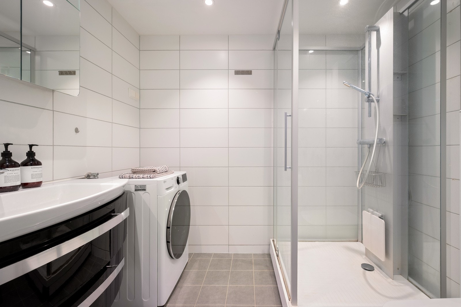 Flislagt baderom med både elektrisk og vannbåren gulvvarme. Det er spotter i taket. Badet er innredet med vegghengt toalett, dusjkabinett, servant med ett-greps blandebatteri og servantskap. Opplegg for vaskemaskin Galleribilde