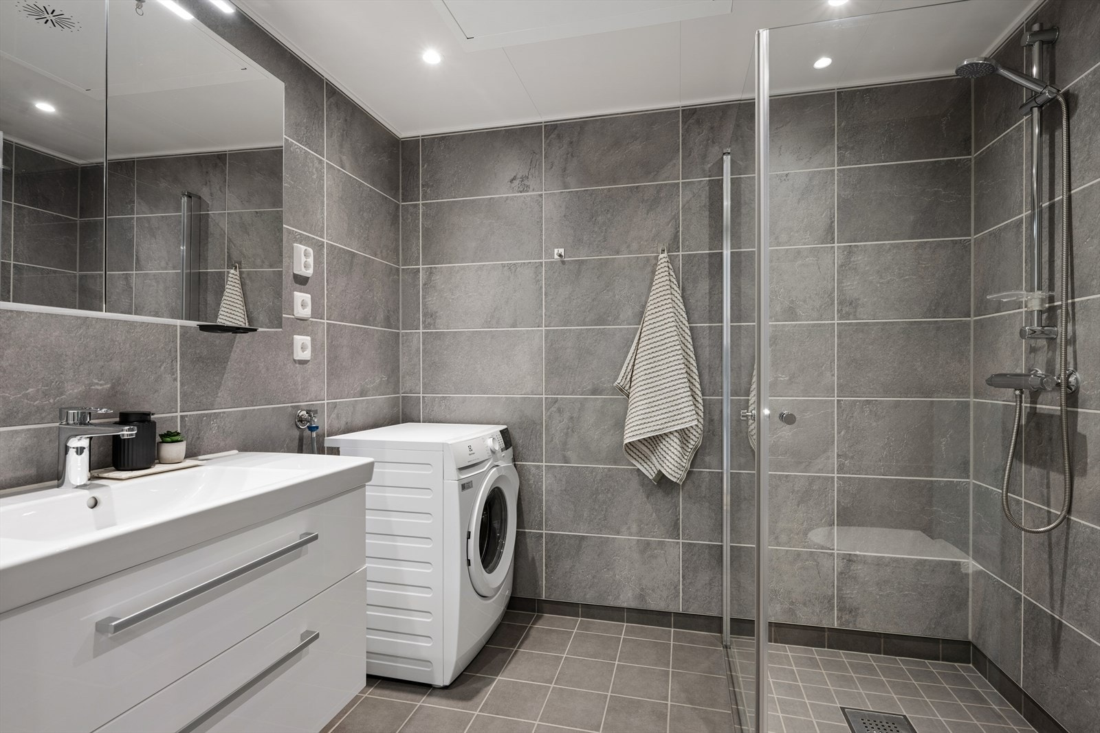 Badet har flislagt gulv, og våtromsplater på veggene. Toalettet er vegghengt og man benytter dusjdører i dusjhjørnet. Badet har opplegg for vaskemaskin. Badet har også vegghengt toalett. Galleribilde