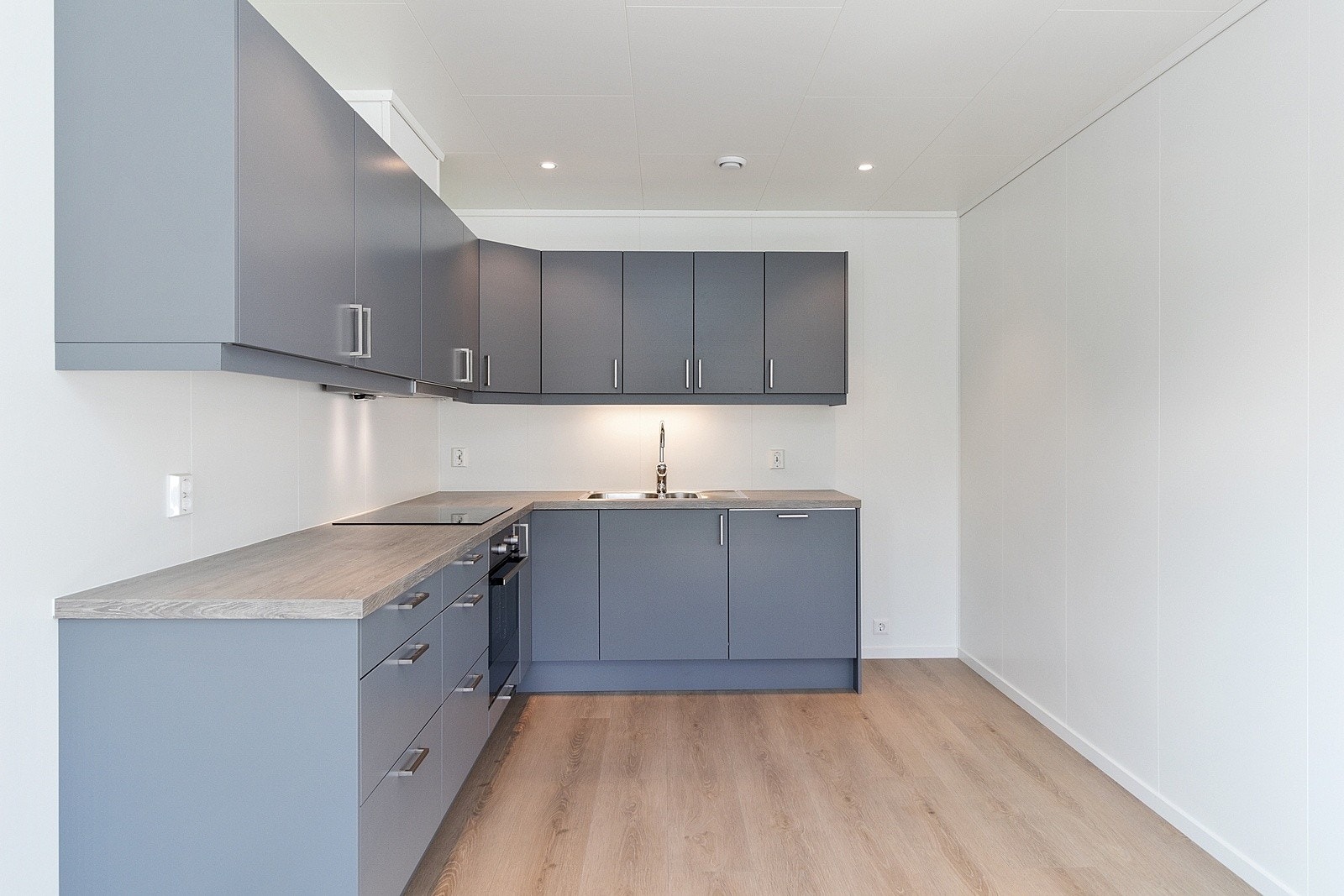 Moderne kjøkken i stilren gråfarge med glatte fronter og slitesterk laminatbenkeplate. Kjøkkenet er komplett utstyrt med integrert stekeovn, platetopp og oppvaskmaskin. Galleribilde