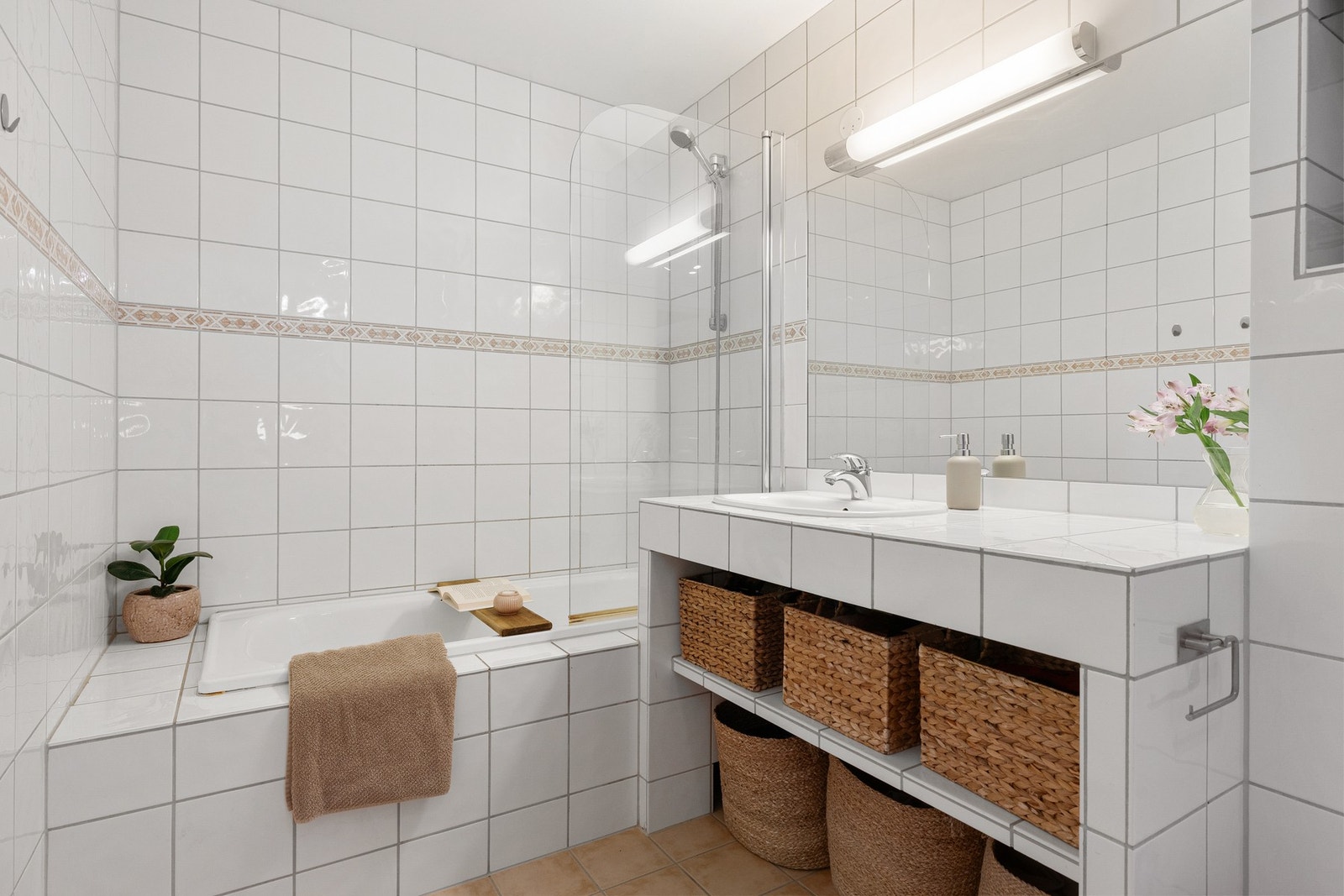 Delikat, flislagt bad med innfliset badekar, romslig servantseksjon med hyller og innfliset speil. Galleribilde