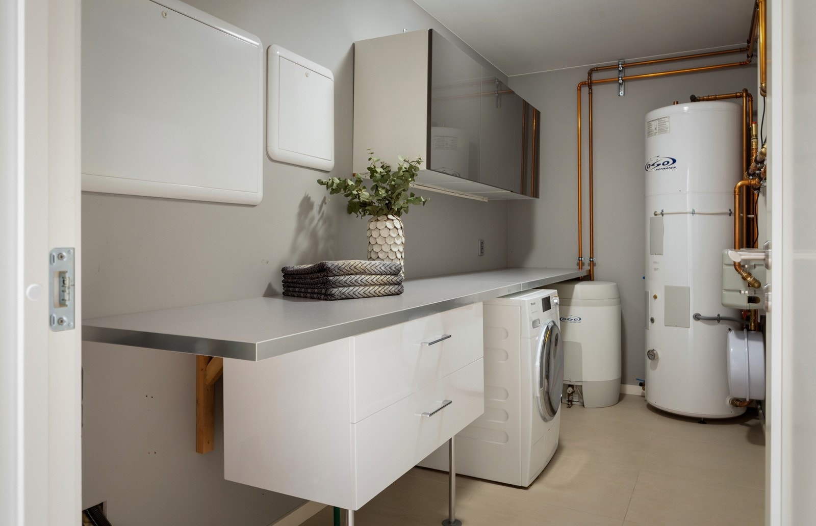 Kombinert vaskerom og teknisk rom. Brettebenk med skuffer, plass til vaskemaskin og ekstra oppbevaring i veggskap. Varmtvannsbereder og system for vannbåren varme. Galleribilde