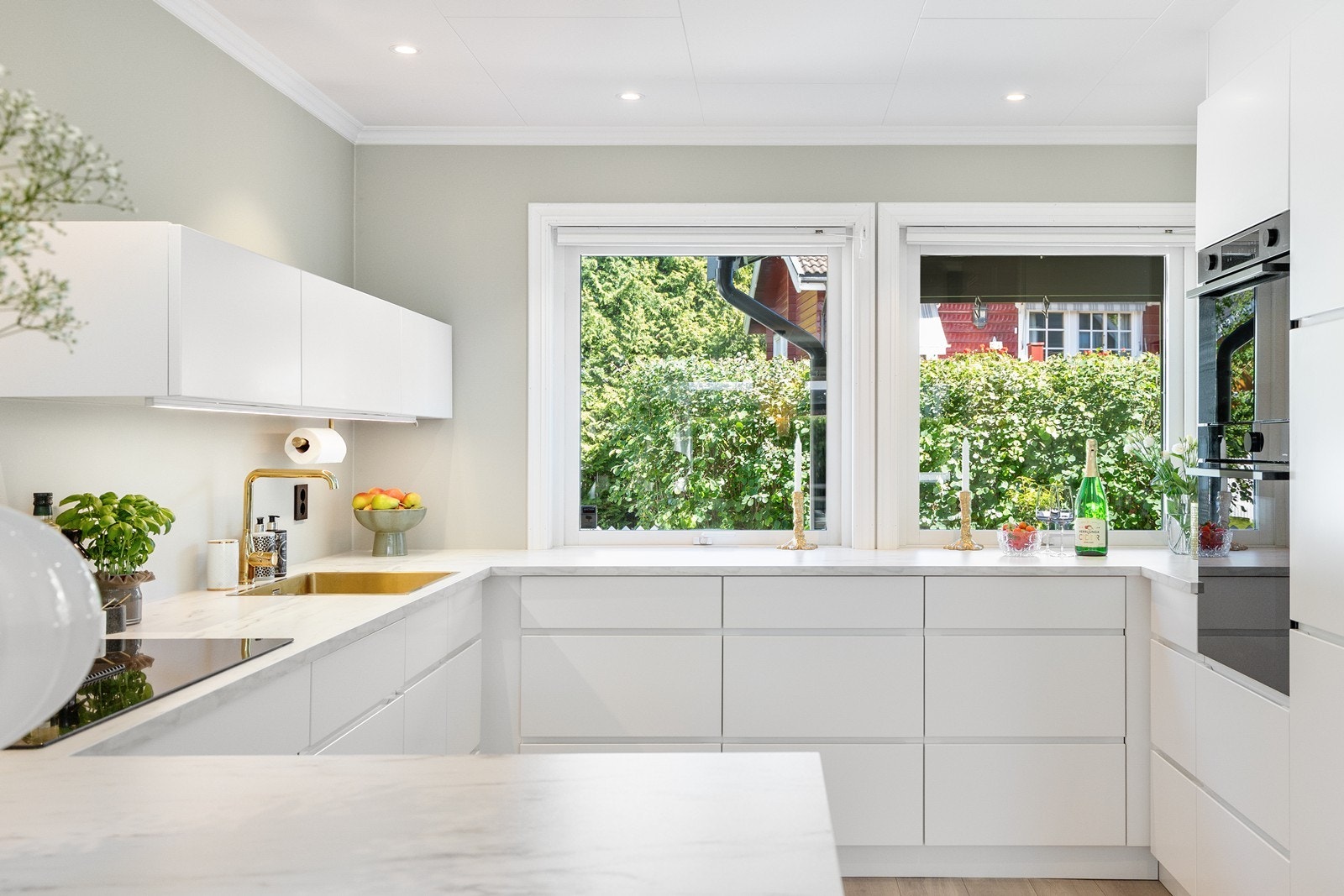 Kjøkkeninnredningen har hvite glatte fronter og hvit laminert benkeplate. Vasken har gullfargede detaljer. Galleribilde