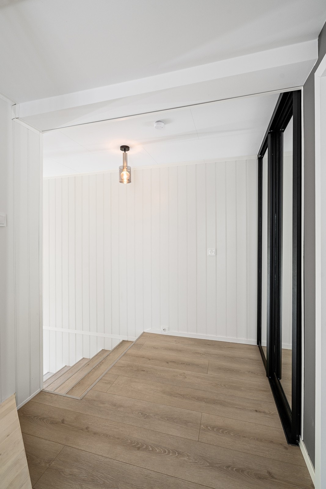 Lys gjennomgang med laminatgulv og malte paneler gir enkel tilgang mellom rommene. Galleribilde