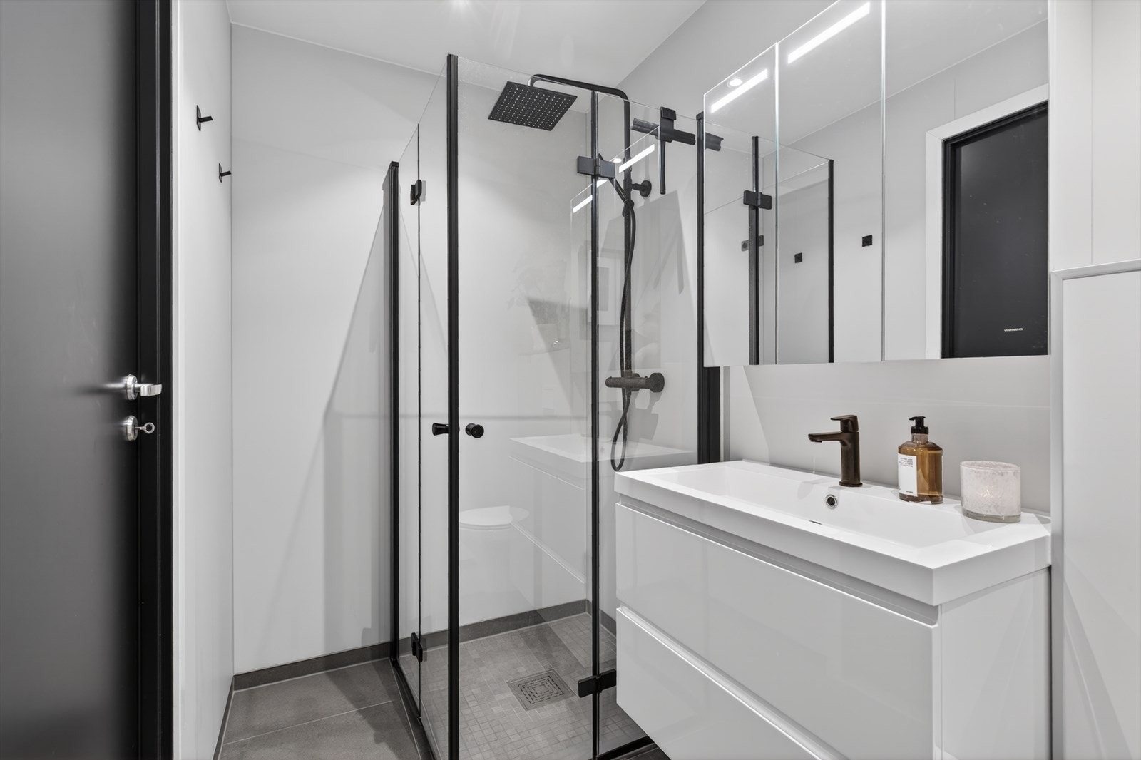 Badet har baderomsplater på veggene, flislagt gulv og et dusjhjørne med innfellbare glassdører. Badet er utstyrt med mekanisk avtrekk og en moderne regnfallsdusj. Galleribilde