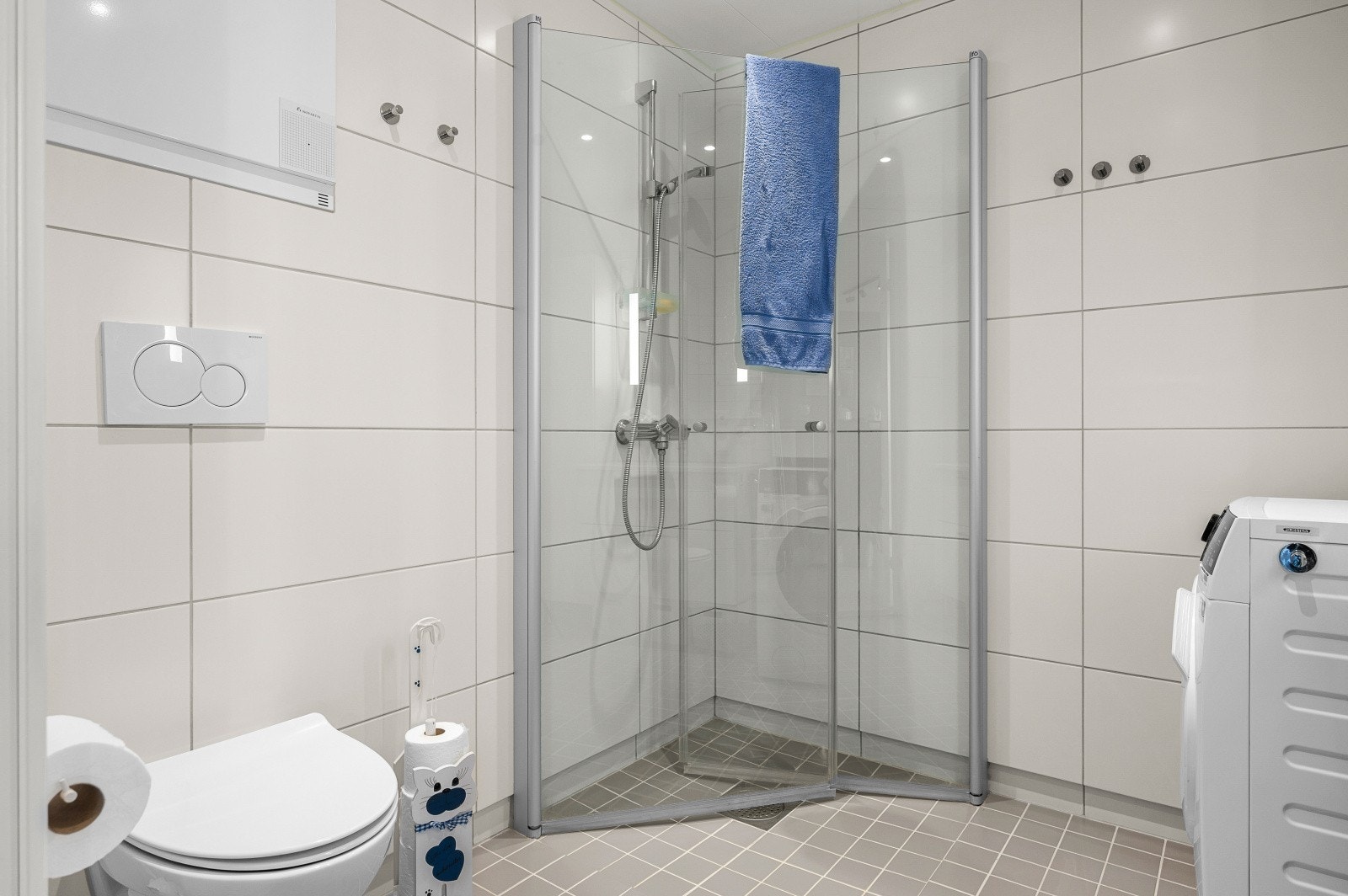 Badet er utstyrt med vegghengt toalett, dusjhjørne med innfellbare dører, servant med baderomsinnredning, speil med integrert belysning og høyskap. Galleribilde