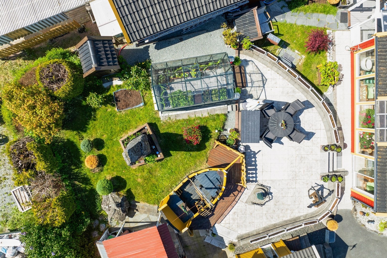 Nydelig opparbeidet uteområde med steinsetting, grønne plener, blomsterbed og flere sitteplasser. Galleribilde