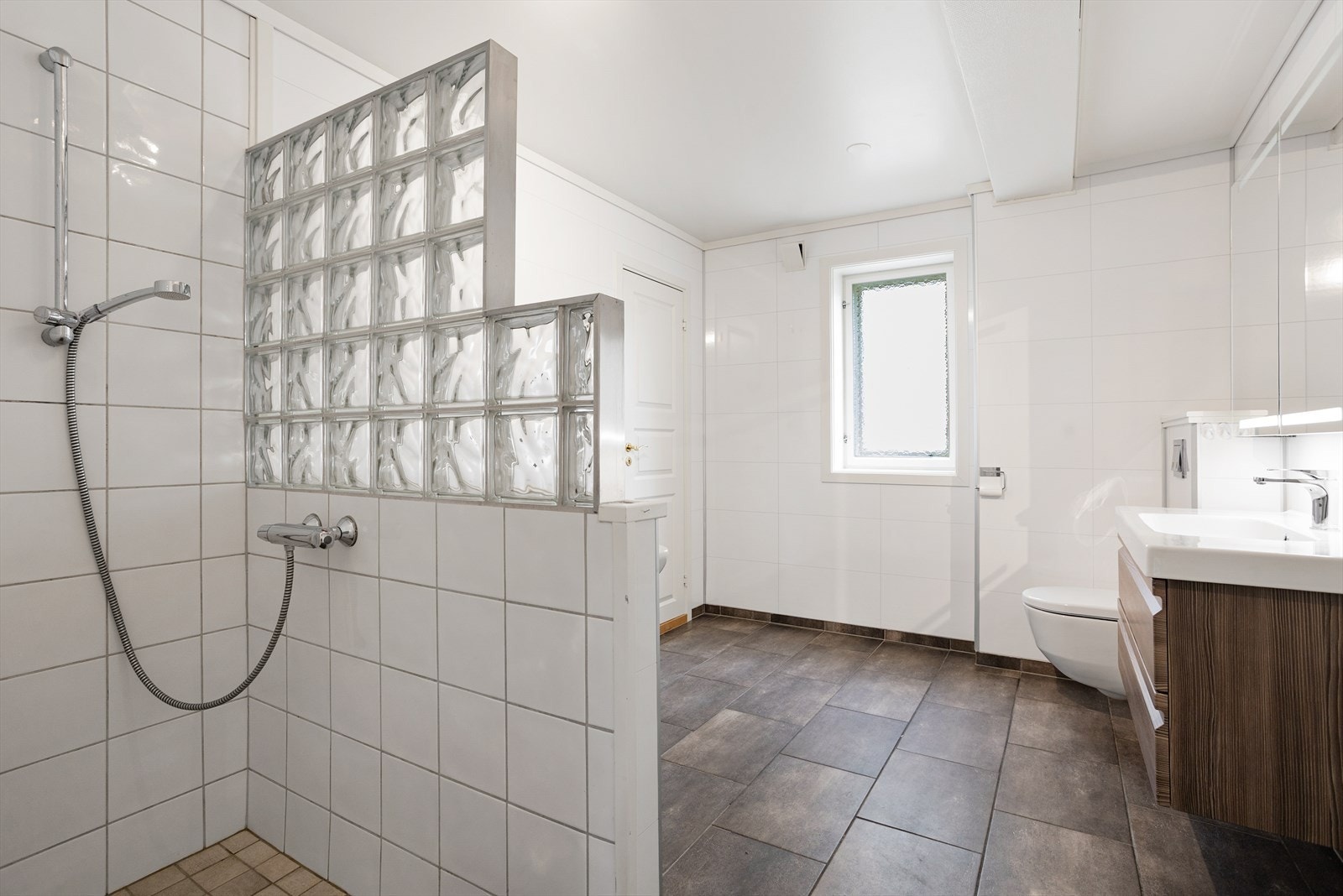 Badet har dusjhjørne med flislagte vegger og en skjermvegg i glassbyggerstein. Galleribilde