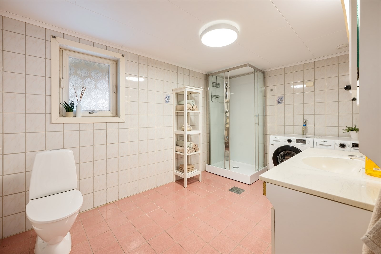Romslig bad kombinert med vaskerom, innredet med dusjkabinett, toalett og opplegg for vaskemaskin. Praktisk løsning med god gulvplass og naturlig ventilasjon via vindu. Galleribilde