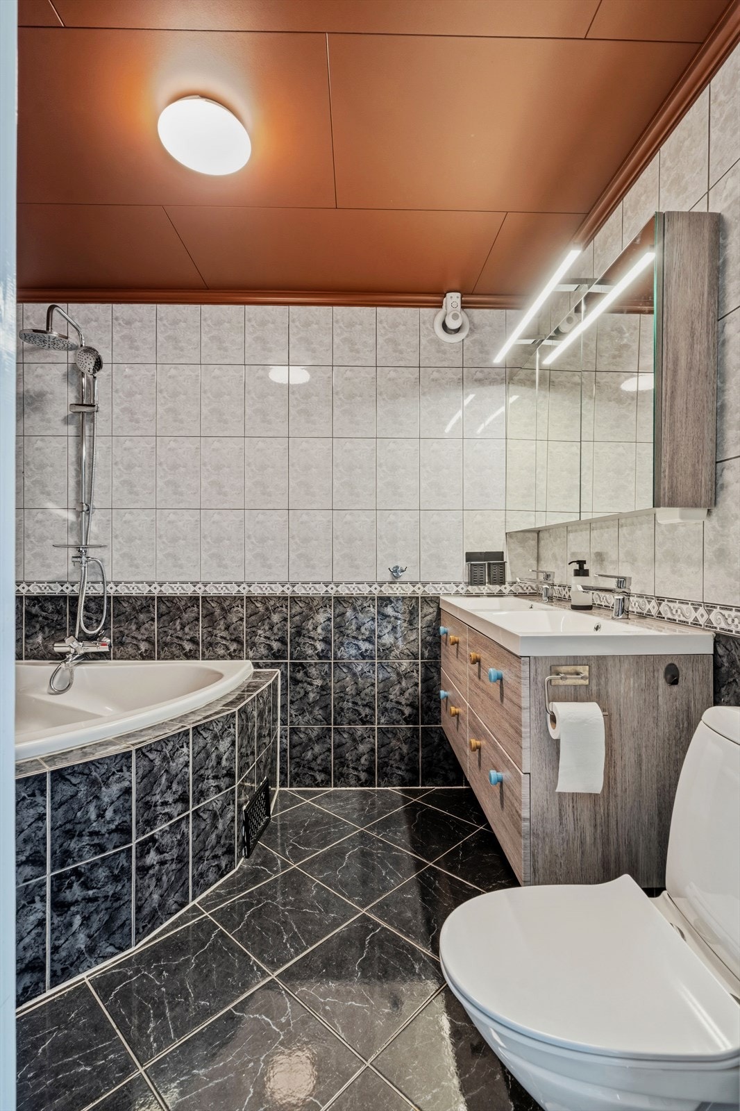 Badet har en elegant kontrast mellom sorte og lyse fliser, samt rikelig med skapplass som dekker familiens behov Galleribilde