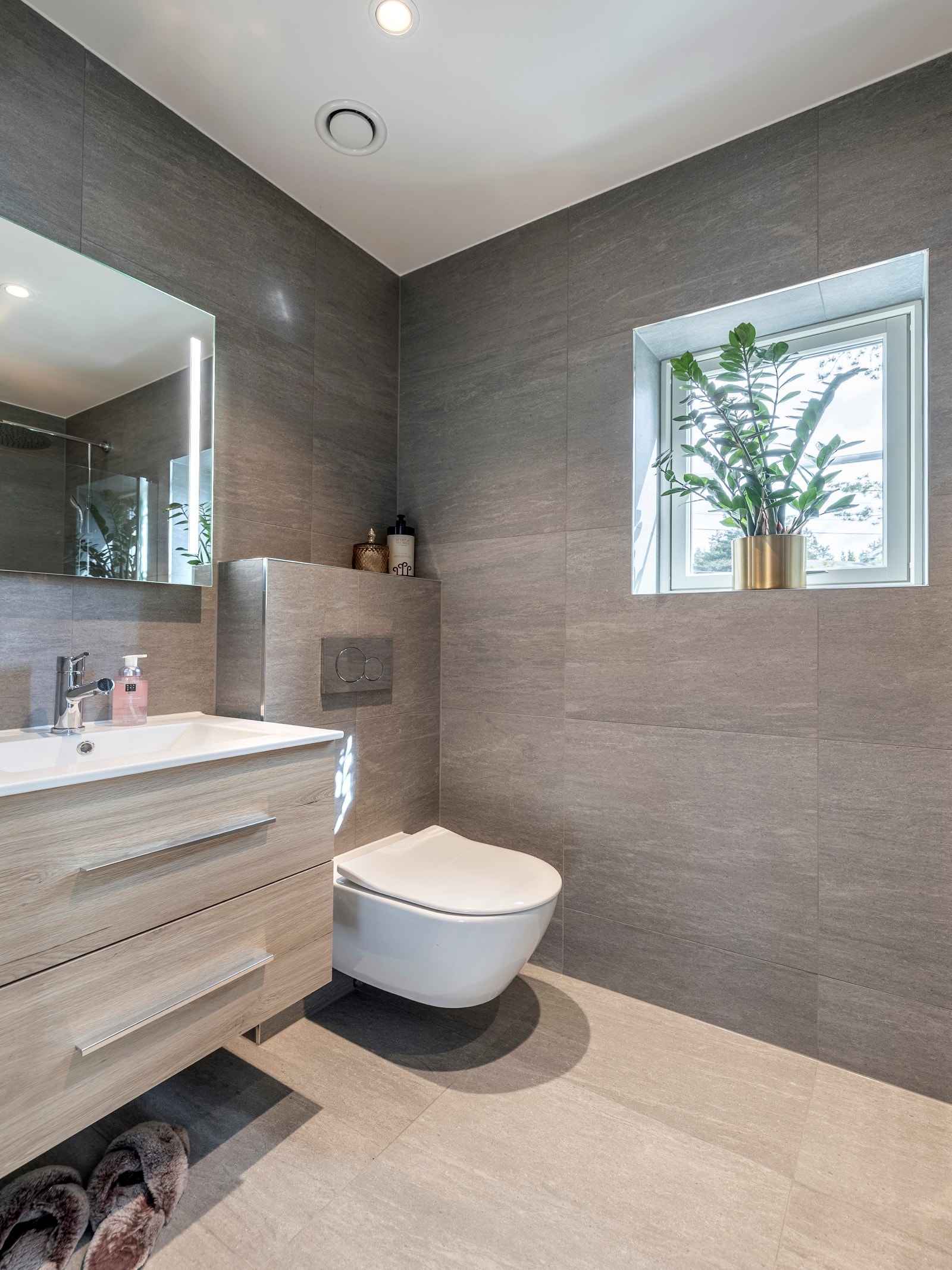 Badet er innredet med servantinnredning, speil med lys på vegg over servant, vegghengt toalett og skjermet dusjhjørne med svingbare glassdører. Galleribilde