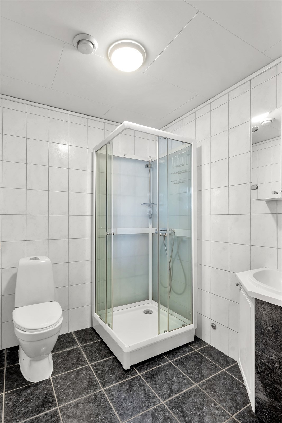Komplett flislagt bad, med praktisk dusjkabinett og baderomsinnredning med oppbevaringsplass. Galleribilde