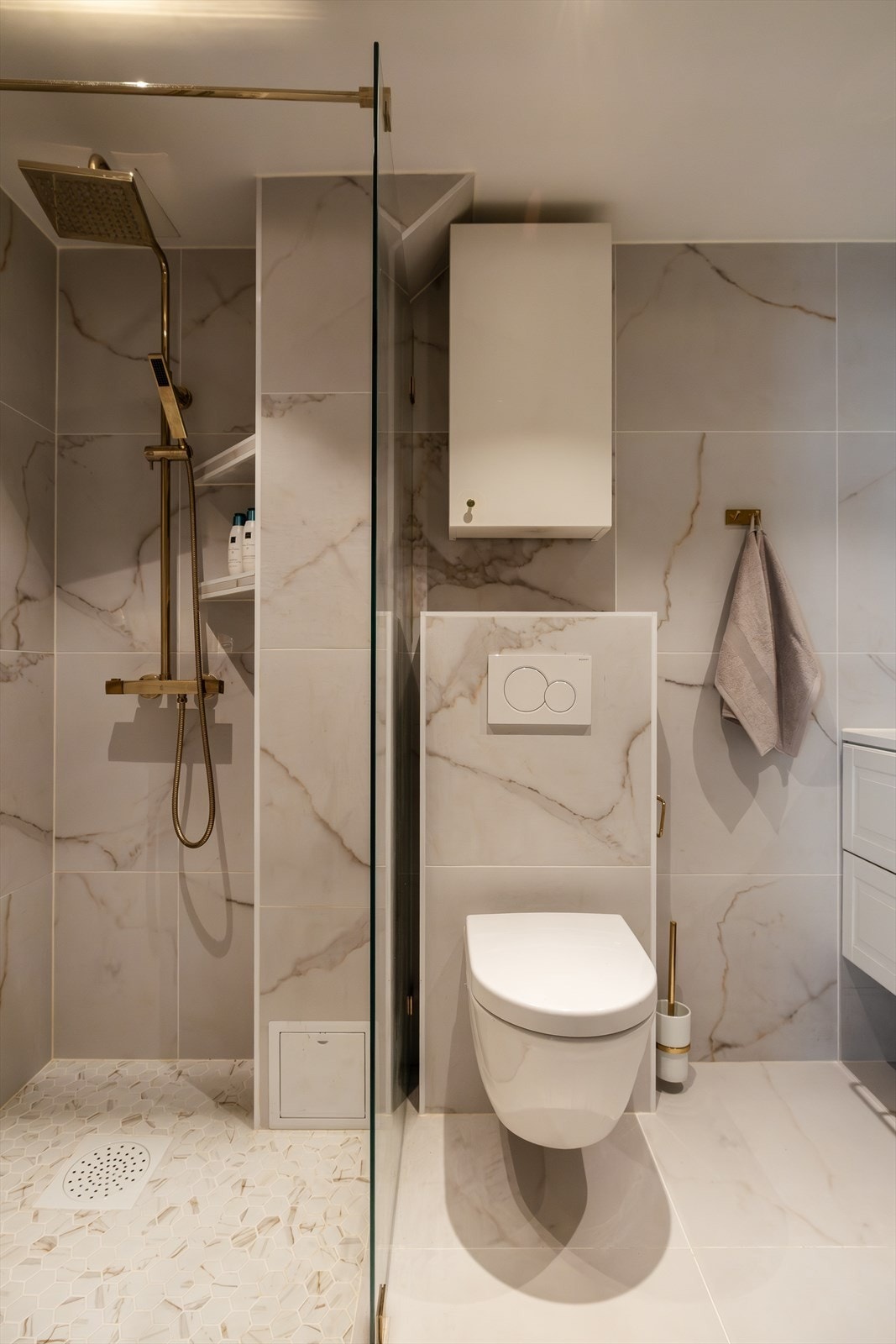Badet er utstyrt med et veggmontert toalett, et dusjhjørne med glassvegg og stang for dusjforheng. Servantinnredning med nisje til grunn vaskemaskin. Galleribilde
