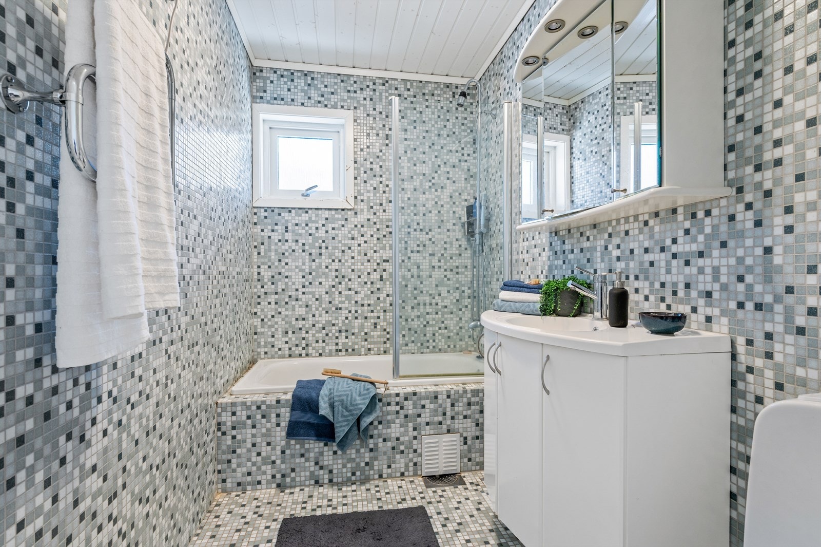 Badet i hovedetasjen er helfliset med mosaikkfliser og utstyrt med badekar, dusjløsning og servantinnredning. Galleribilde