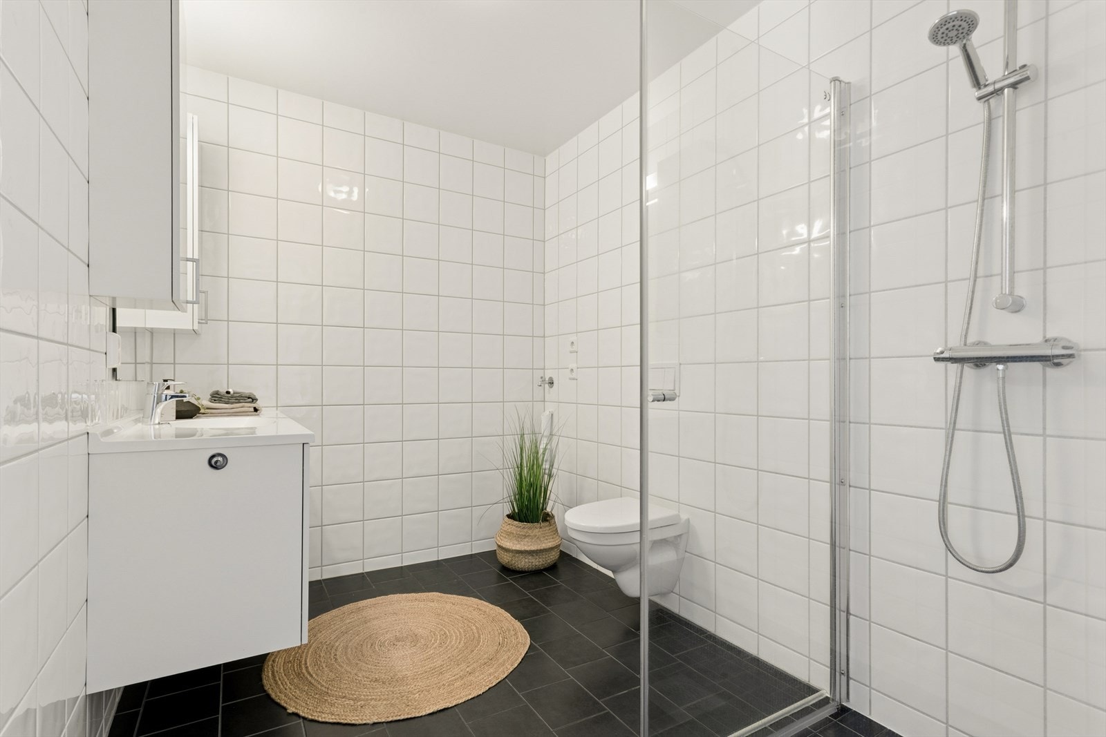 Delikat bad med flislagte overflater, dusjhjørne, vegghengt toalett og opplegg for vaskemaskin. Galleribilde