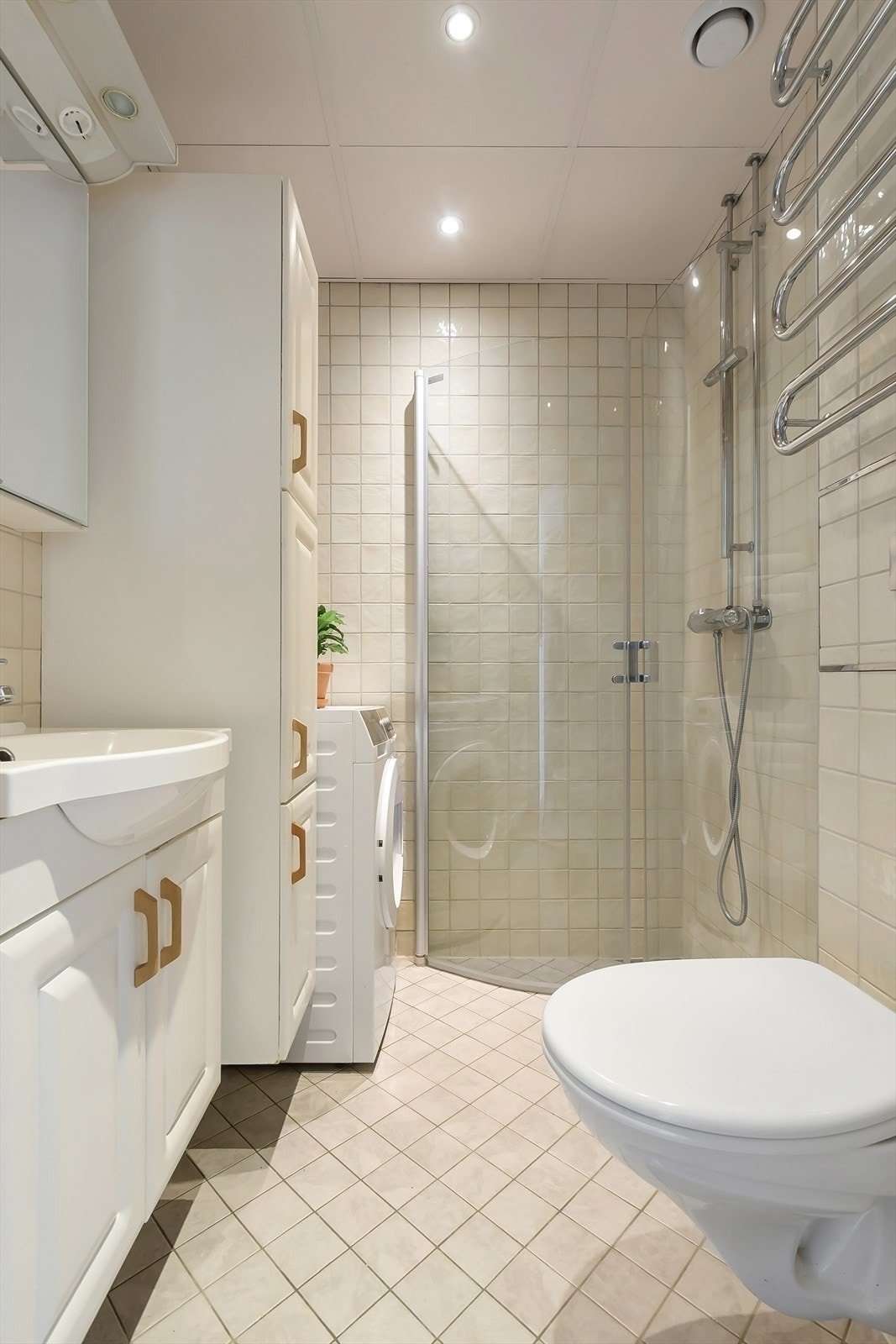 Badet er innredet med dusjhjørne med glass dører, vegghengt toalett og innredning med nedsunket servant med speilskap. Det er opplegg for vaskemaskin. Galleribilde