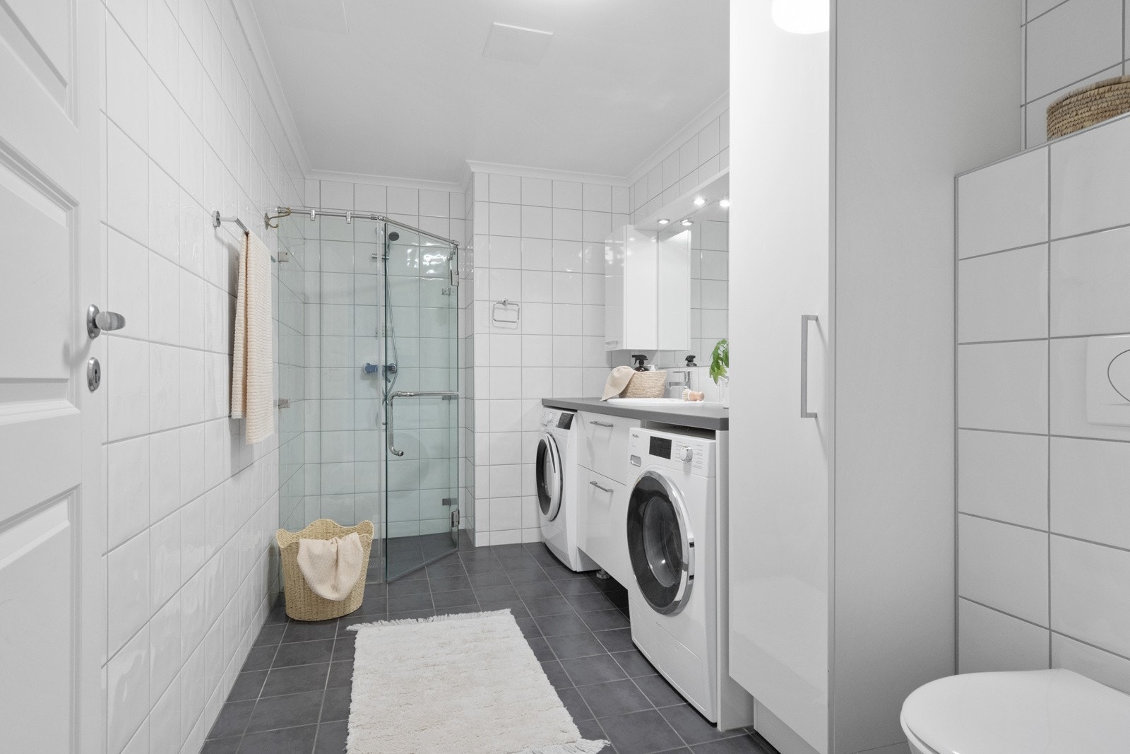Det andre badet er klassisk, med hvite veggfliser og grå gulvfliser over gulvvarme. På hver side av skuffeseksjonen er det opplegg for vaskemaskin og tørketrommel. Galleribilde