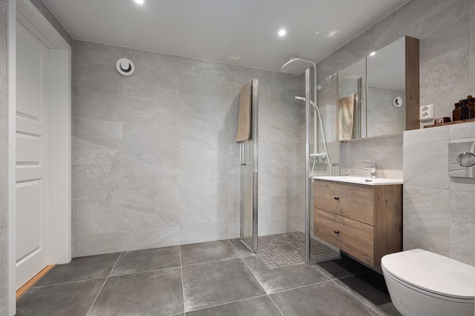 Badet ble rehabilitert av Mika Byggtjenester AS i 2025. Store fliser på vegger og gulv gir et stilrent uttrykk, mens malt himling og innfelte downlights bidrar til en lys og behagelig romfølelse. Galleribilde