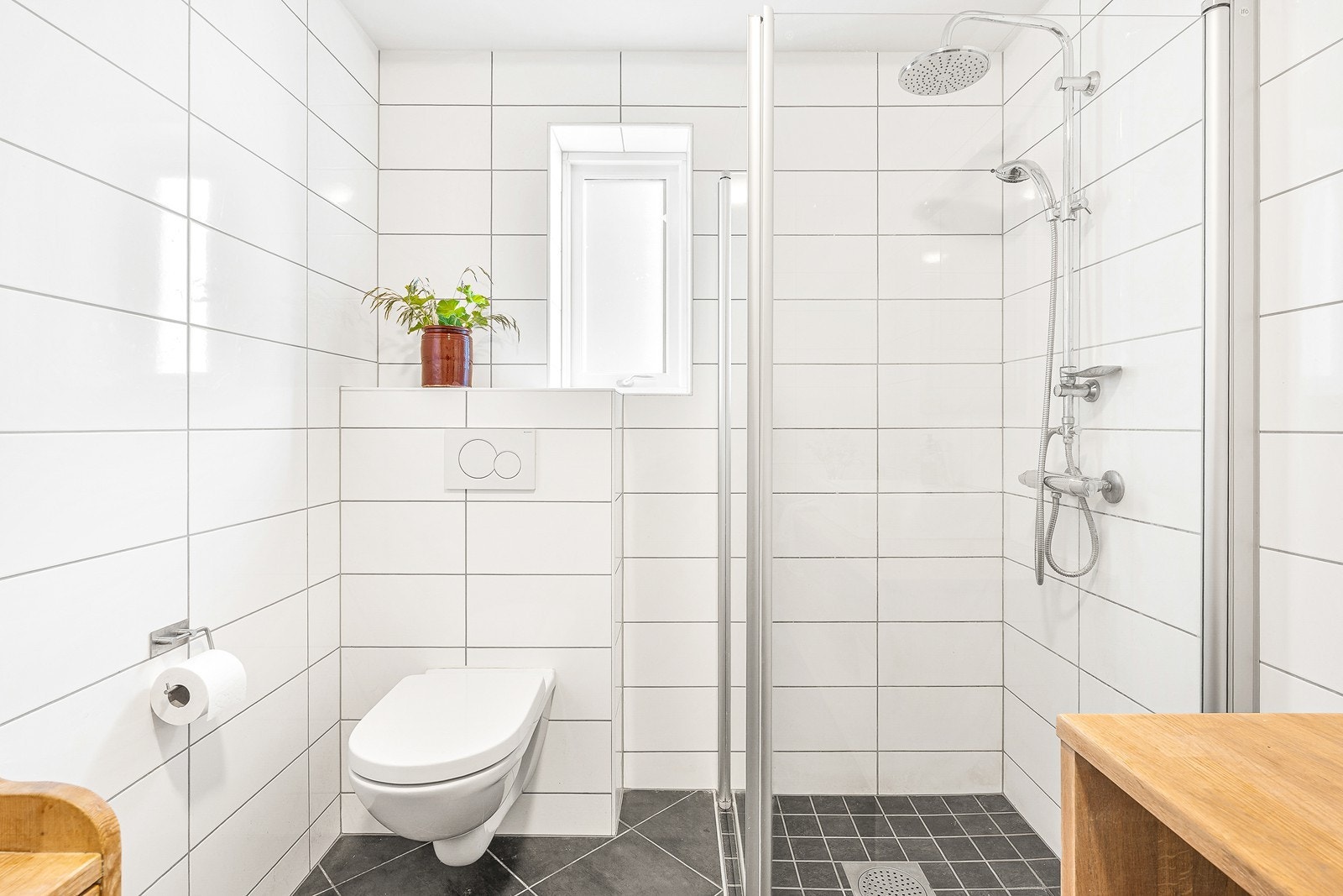 Badet er helfliset og pent, med mørke fliser på gulv og hvite fliser på vegger Galleribilde