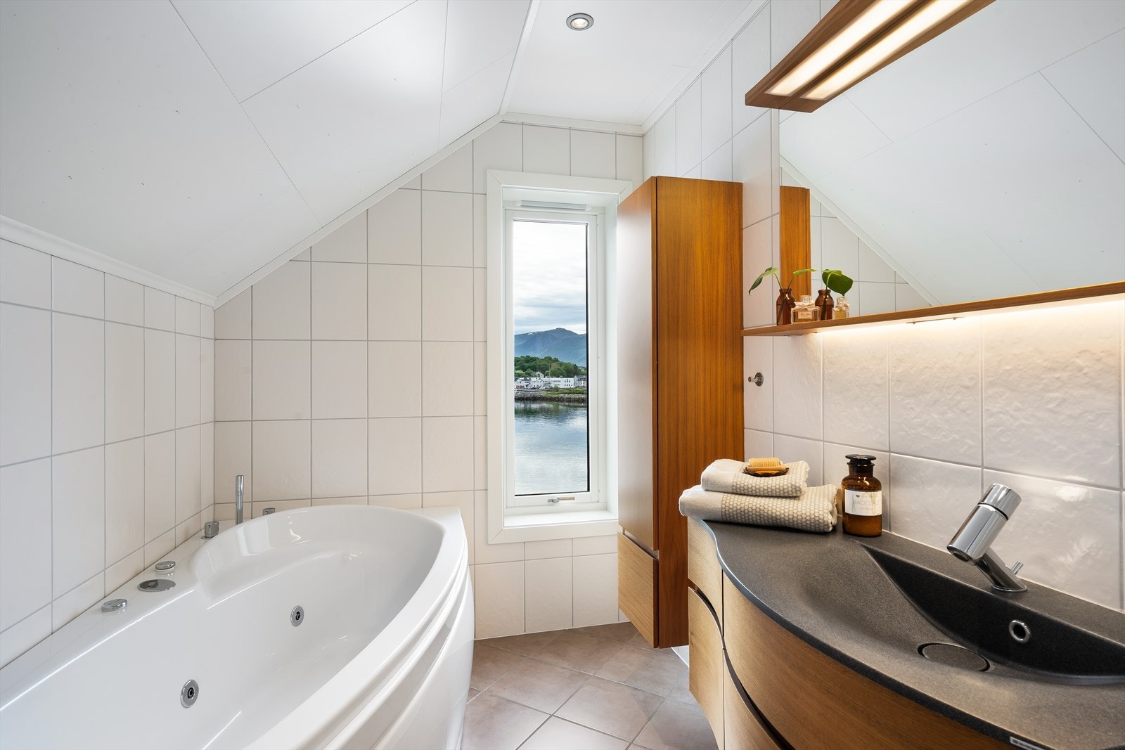 Badet har et flislagt bad med vannbåren varme i gulv og rommet har innredning med underskap, servant, speil og høyskap. Galleribilde