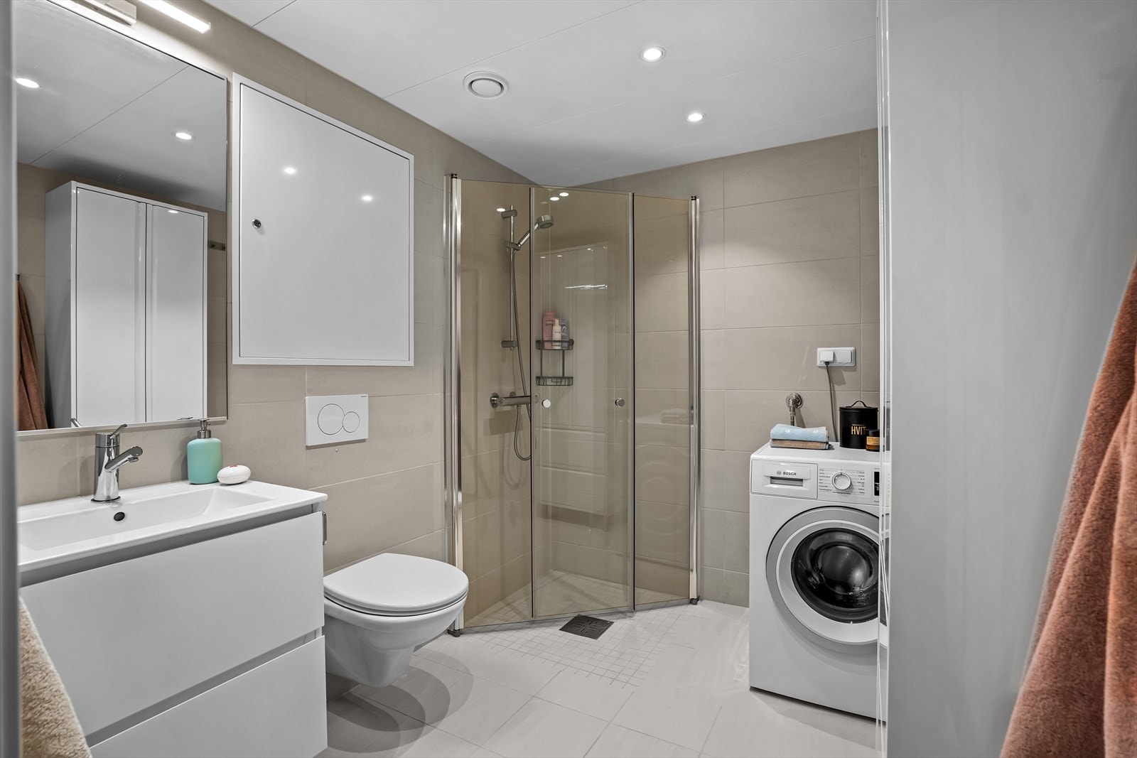 Badet er delikat og moderne med vegghengt toalett, dusjdører i herdet glass og en praktisk baderomsinnredning med malte fronter og heldekkende servant. Galleribilde