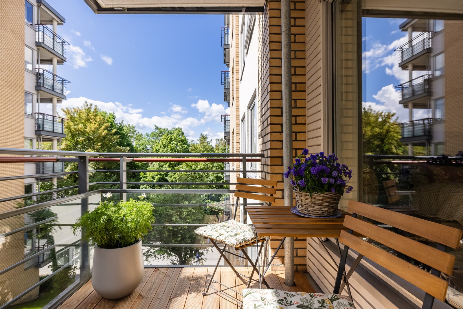 Balkongen er overbygget, har terrassebord fra 2025 på gulv og rekkverk av metall og glass. Galleribilde