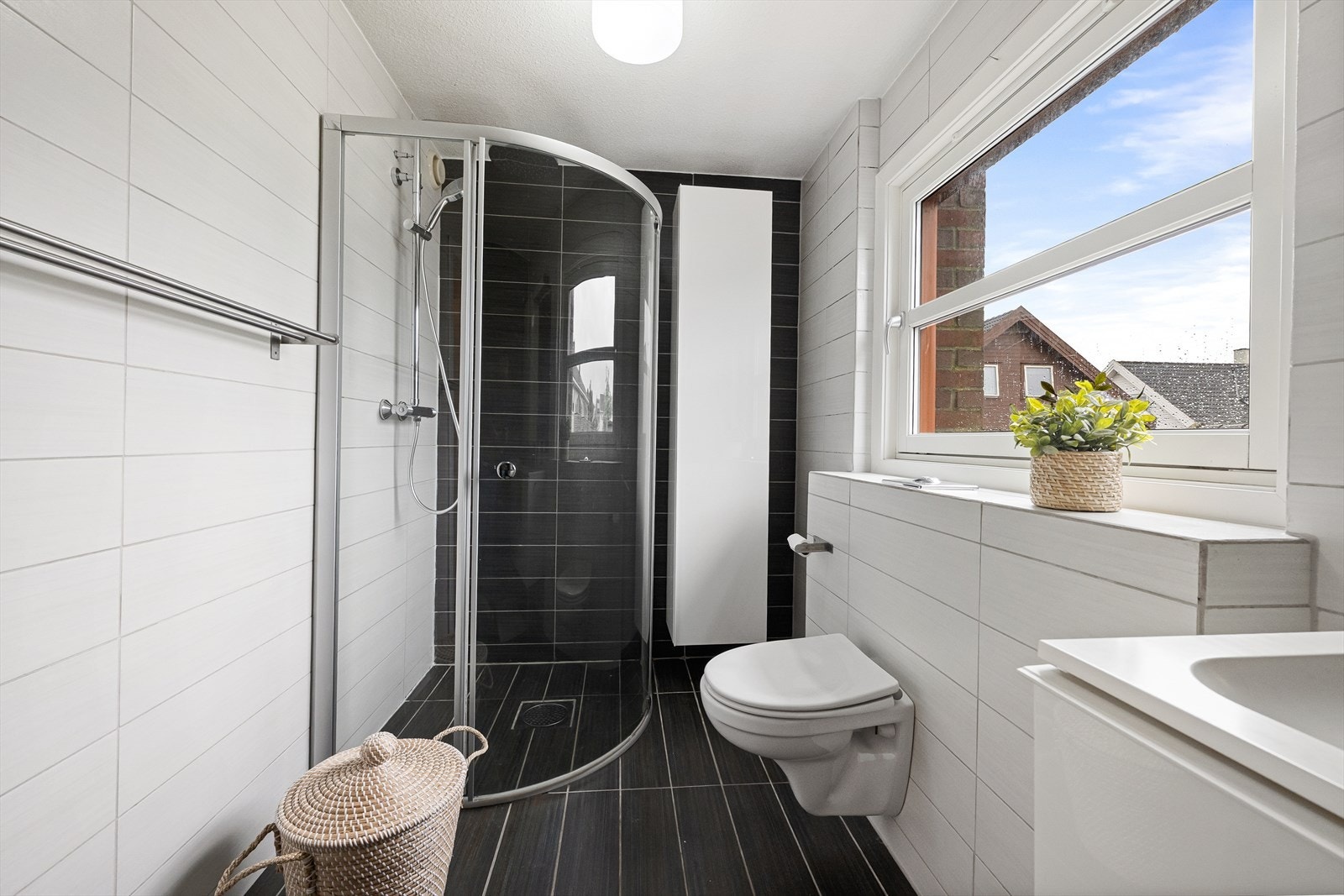 Badet er utstyrt med dusjhjørne med glassvegger, vegghengt toalett og servantinnredning. Galleribilde