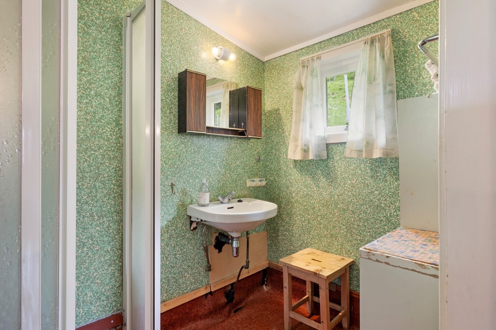 Badet er utstyrt med dusjkabinett og servant. Rommet har overflater frå 70-tallet med behov for modernisering. Galleribilde