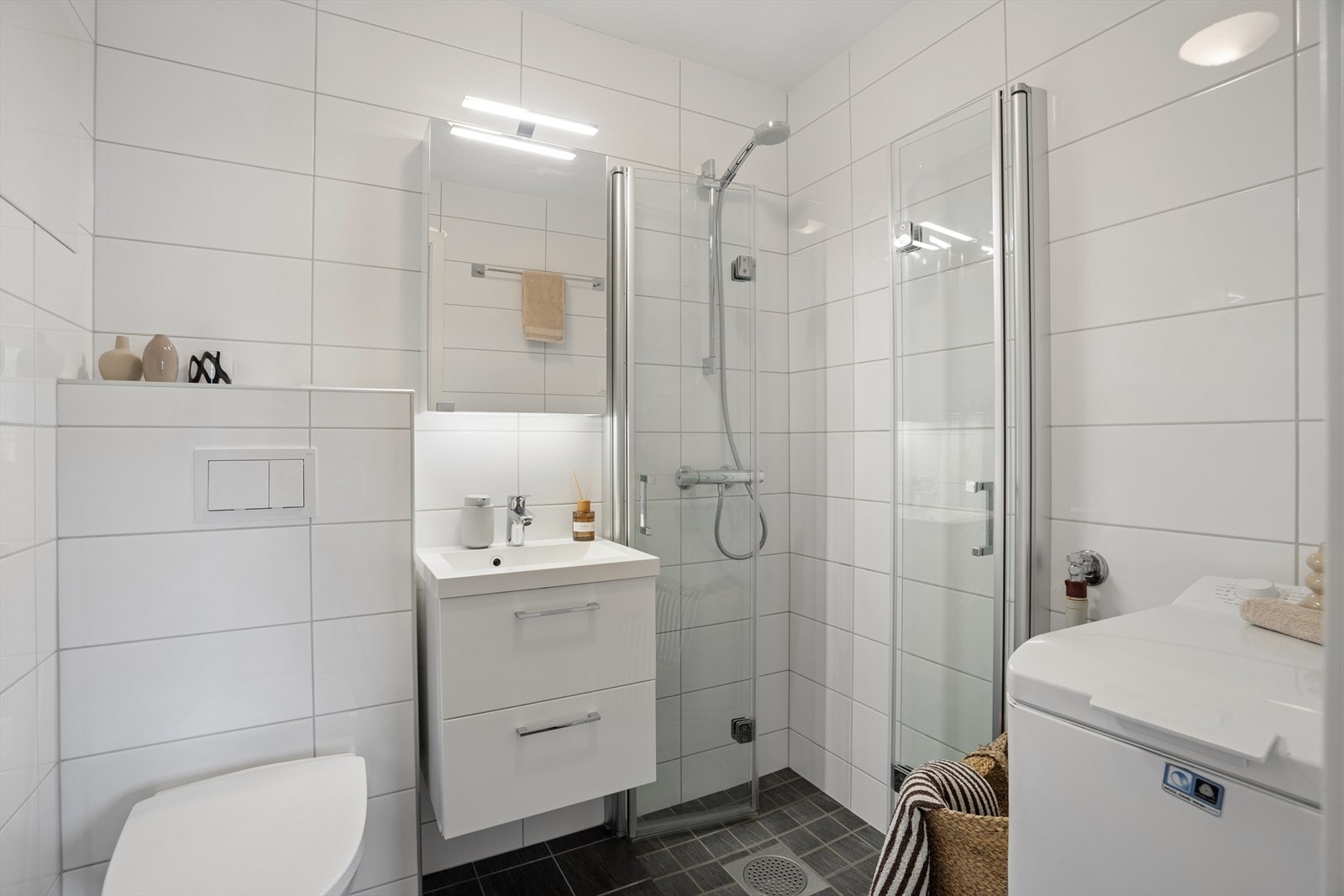 Badet er innredet med servantinnredning, vegghengt speilskap, vegghengt toalett og dusjhjørne med glassvegger, og har i tillegg opplegg for vaskemaskin. Galleribilde